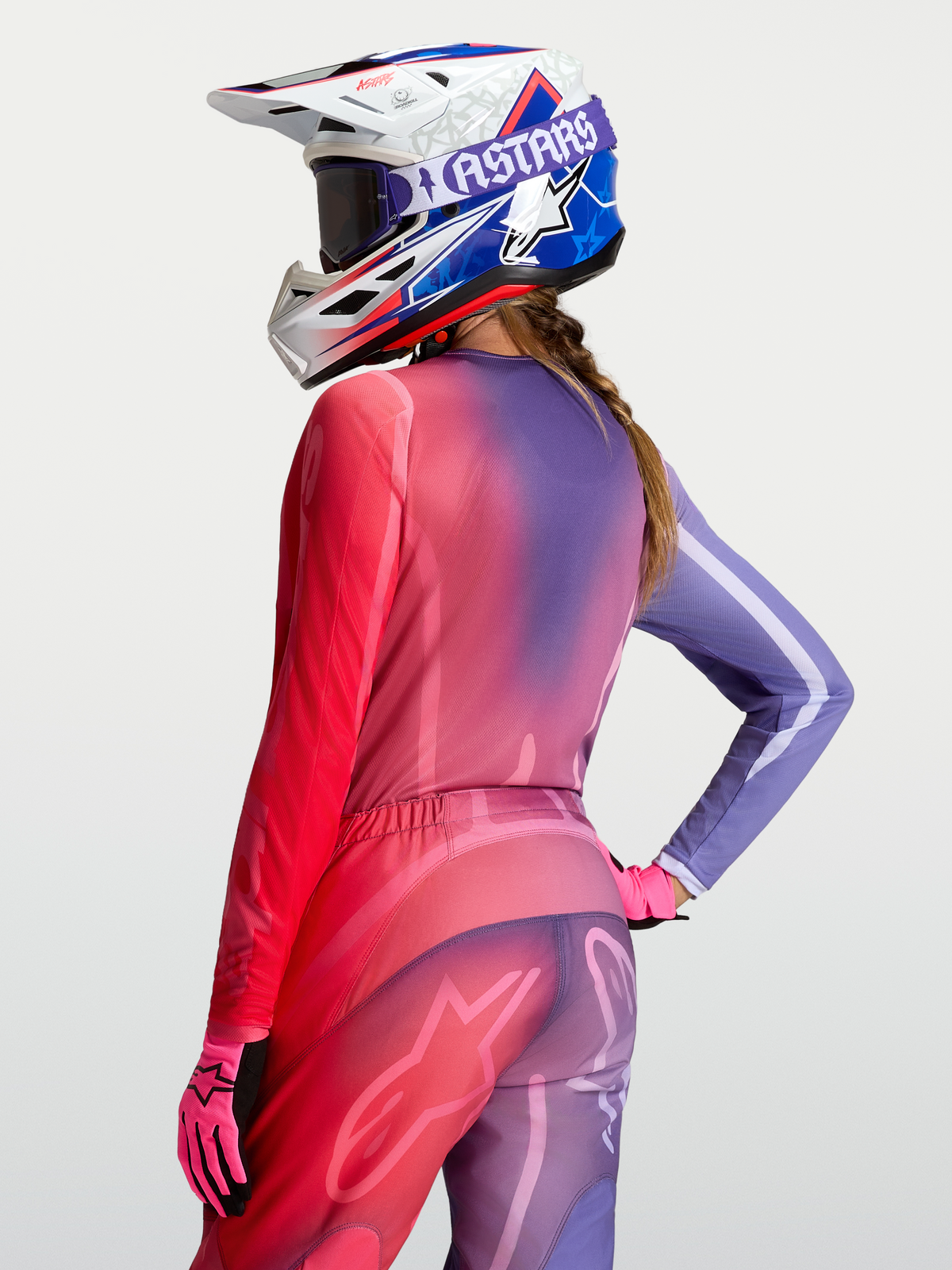 Maillot Stella Fluid Kepler Alpinestars, maillot de motocross pour femme, dégradé violet et rouge, poly-tissu respirant porté par une pilote avec casque et gants coordonnés, vue arrière
