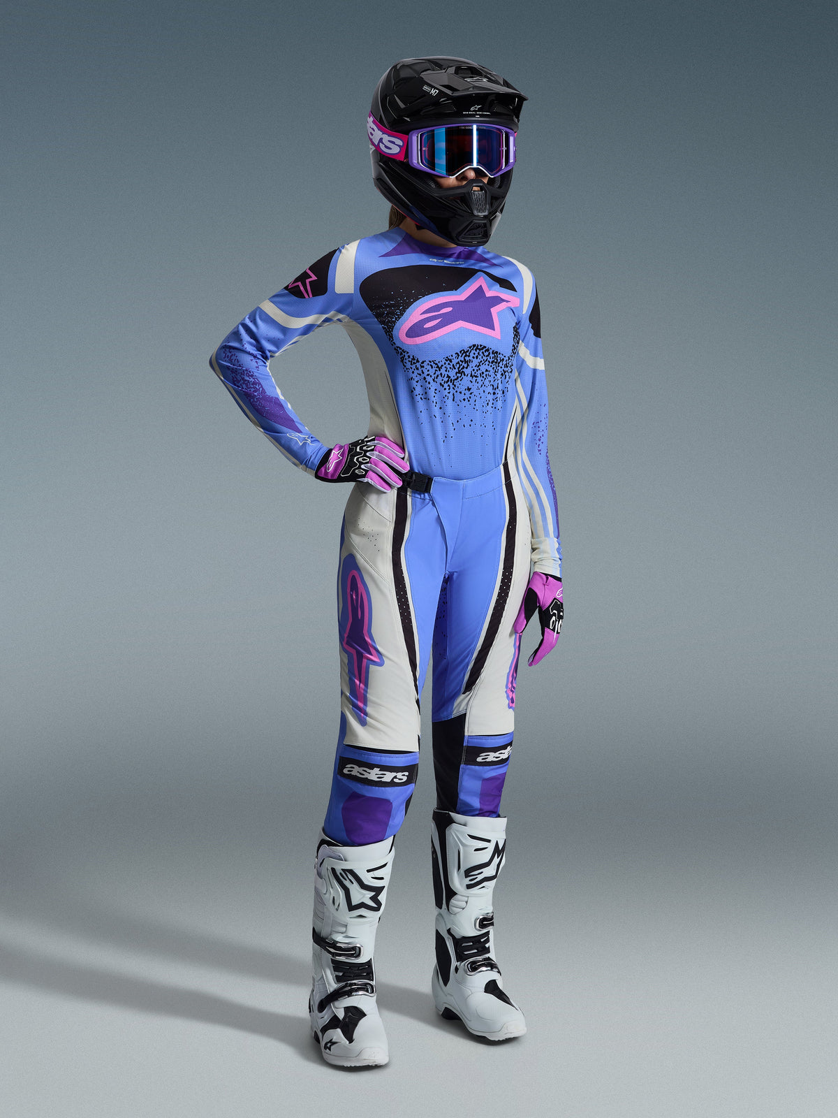 Ensemble d'équipement Alpinestars 2026 Stella Techstar Nomur, tenue de motocross pour femme comprenant un maillot bleu clair avec logo Astar rose, un pantalon assorti avec empiècements blancs et noirs, un casque noir avec des lunettes roses et violettes, des gants roses et des bottes de motocross blanches