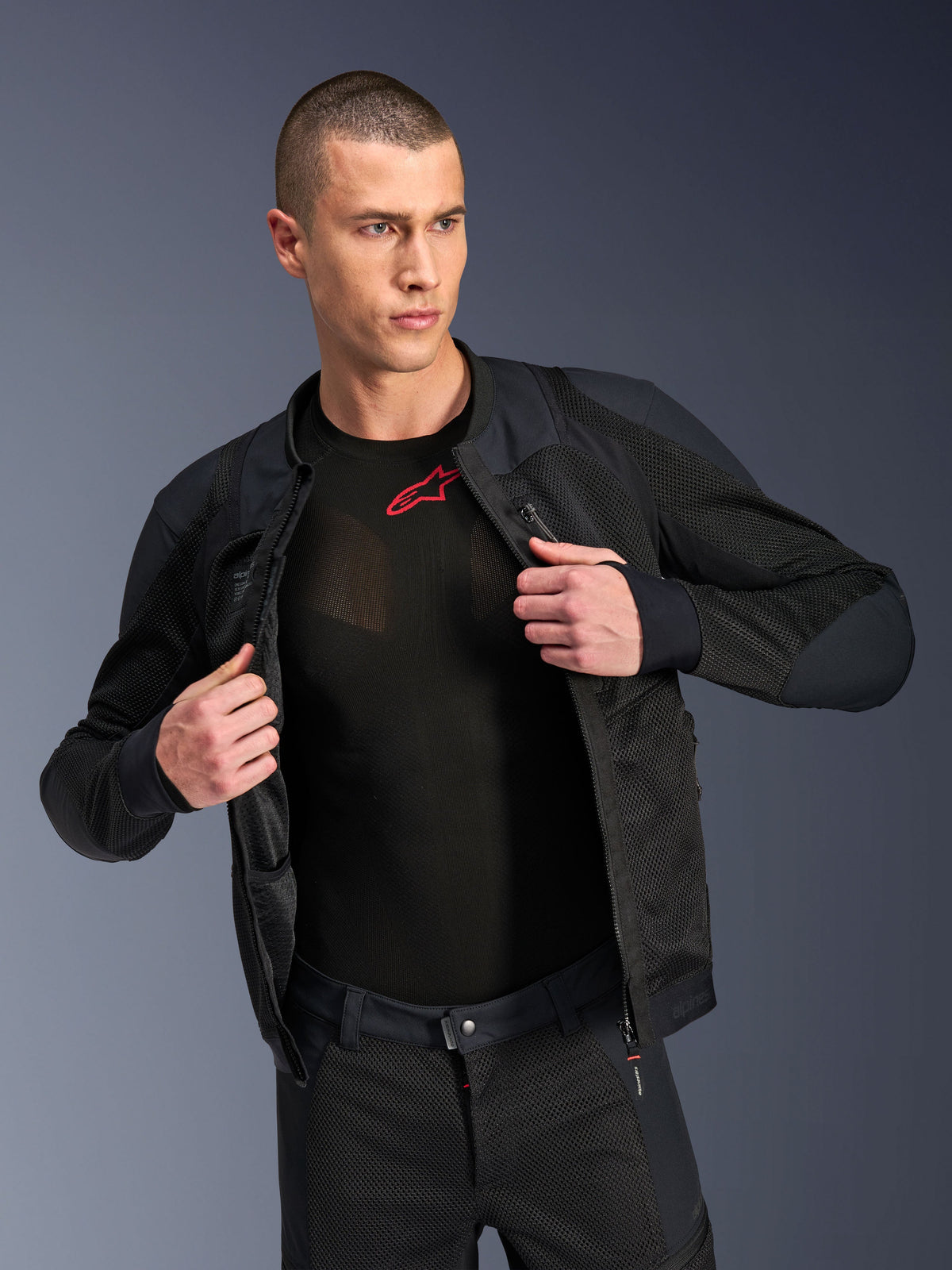 Alpinestars Troop-Air Pro Jacket, Black, premium technical armored air jacket with mesh construction, worn open over a black base layer with a red logo, paired with matching mesh motorcycle pants, urban contemporary riding style