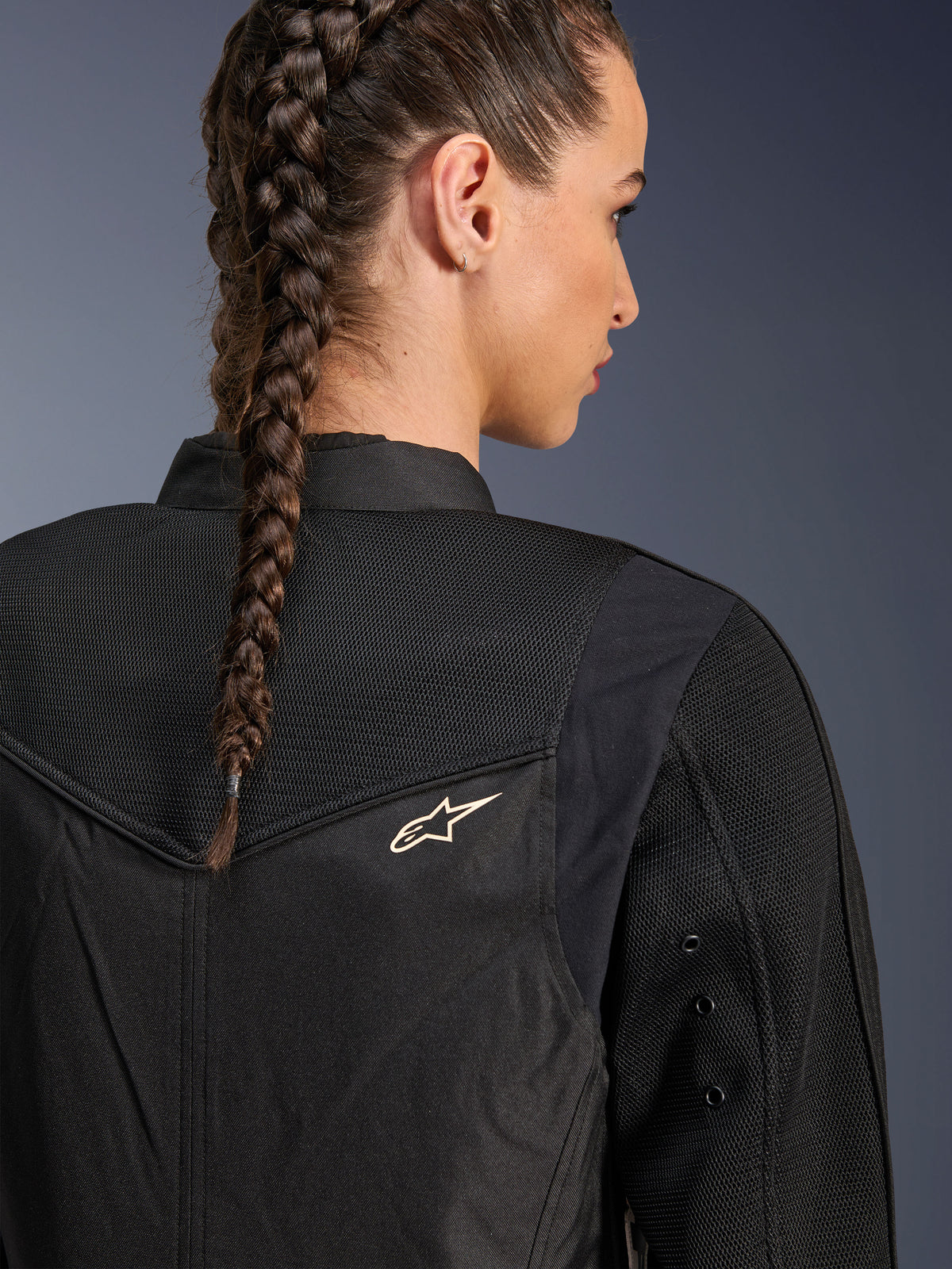 Veste Alpinestars Stella T-Dyno Air, veste de moto noire pour femme, vue arrière rapprochée montrant des panneaux en maille 3D sur l'empiècement et le haut du dos pour la circulation de l'air, avec un petit logo étoile blanc, portée par un mannequin aux cheveux tressés