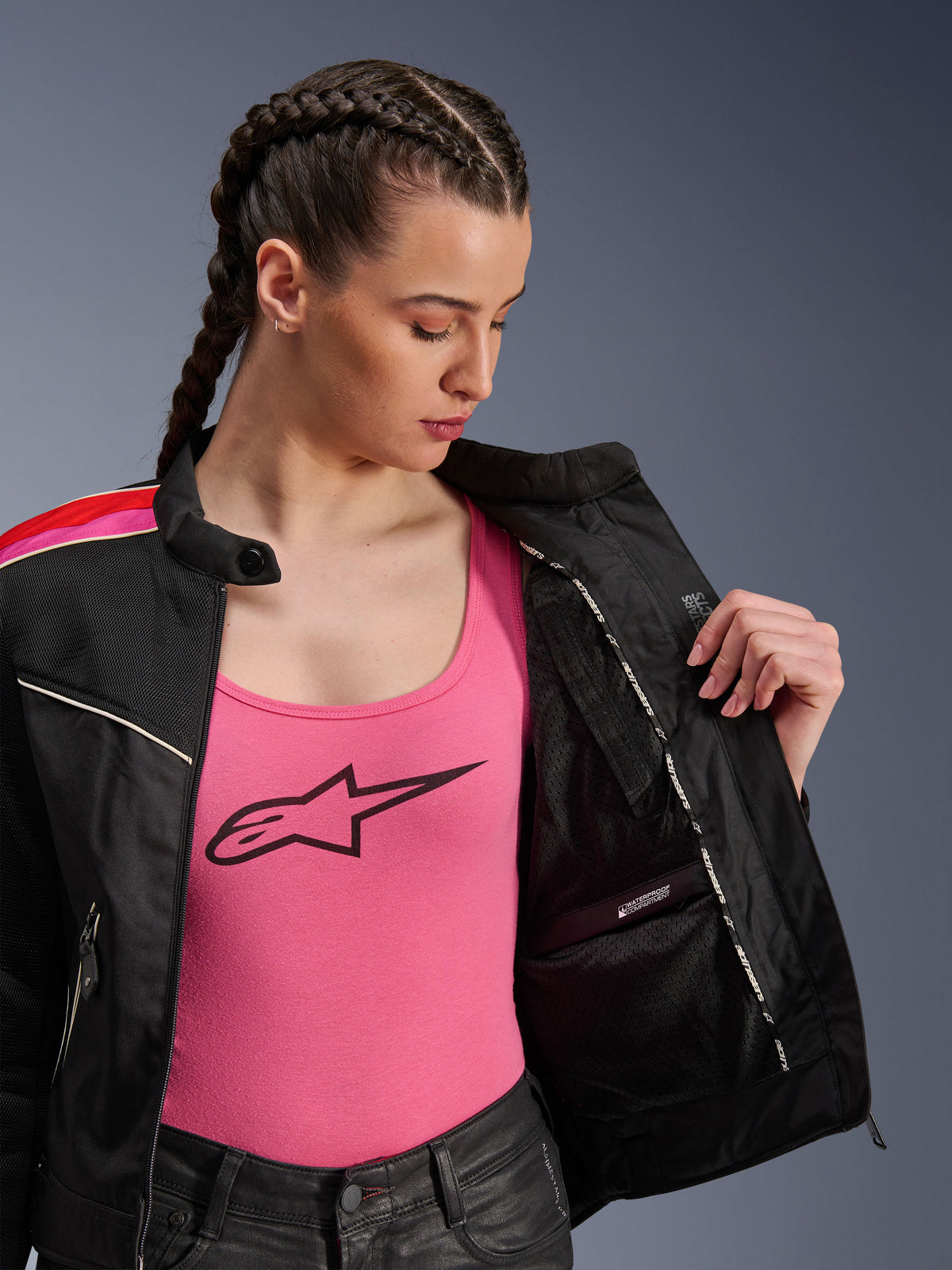 Female rider wearing the Alpinestars Stella T-Dyno Air Jacket in Black Bright Red Fuchsia, shown partially open to reveal the internal waterproof compartment, worn over a pink logo tank top, highlighting the breathable mesh panels and tailored biker fit.