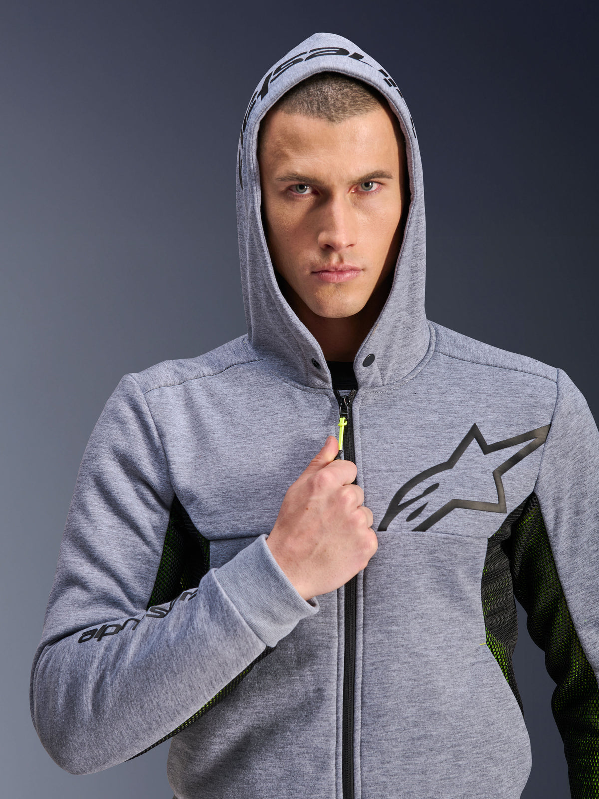 Alpinestars Chrome Air Sport Hoodie, gris chiné noir, sweat à capuche de moto porté par un homme avec la capuche relevée, logo étoile noir sur la poitrine, tirette de fermeture éclair jaune néon, panneaux latéraux en mesh pour la ventilation, style urbain