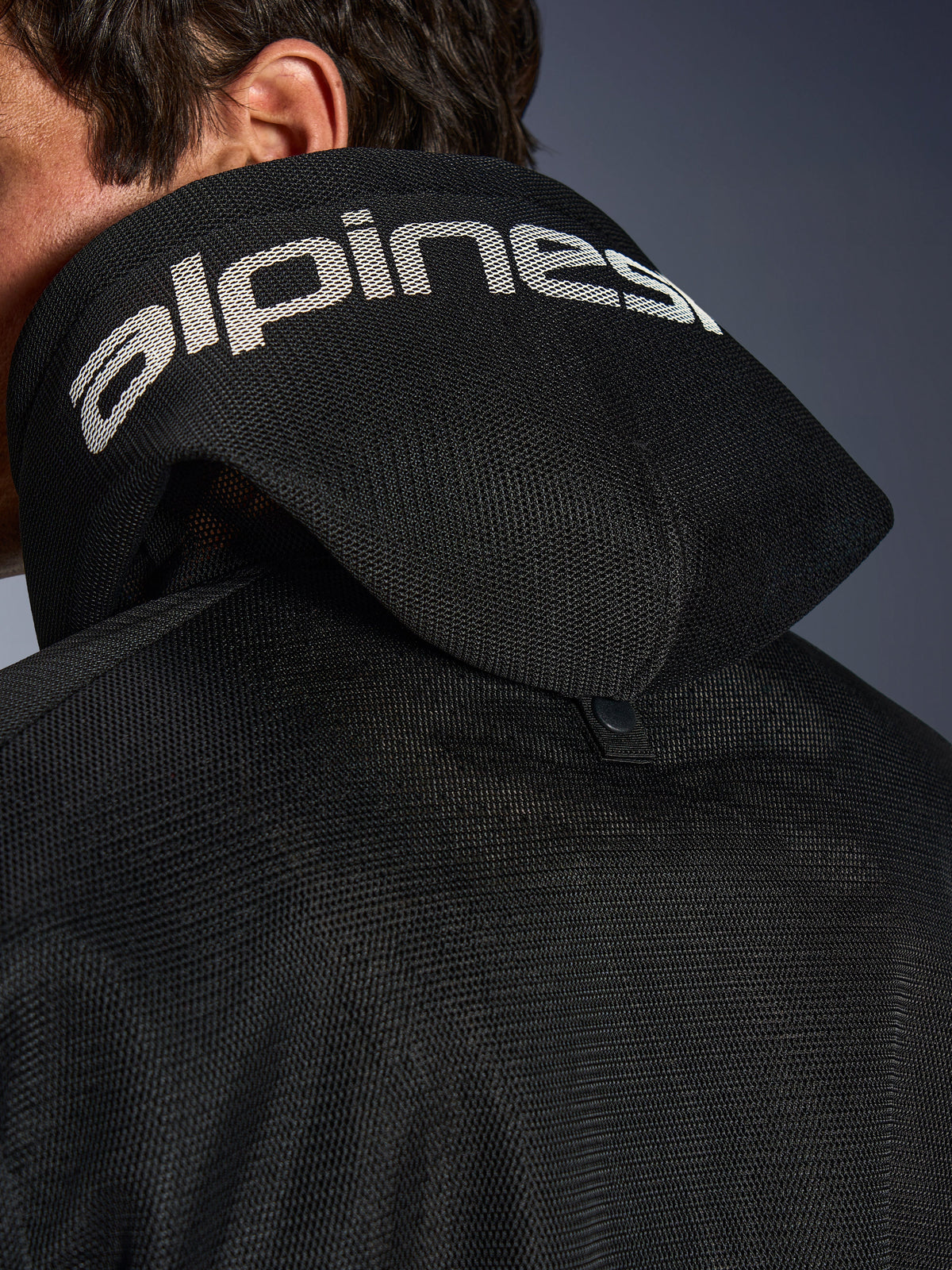 Alpinestars Chrome Superairflow Hoodie, noir, vue détaillée de la capuche en maille 3D avec marquage Alpinestars blanc sur le dessus, bouton-pression de stabilisation arrière, équipement de moto en textile ventilé pour chaleurs extrêmes
