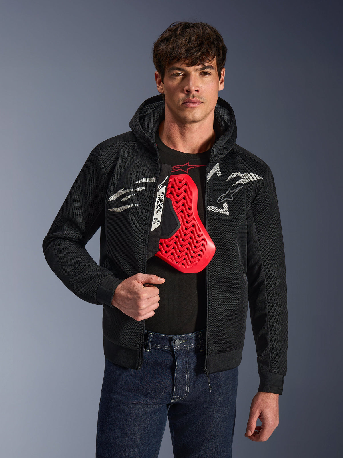 Alpinestars Chrome Superairflow Hoodie en noir, avec logos Astars blancs et gris, porté par un mannequin homme avec une protection de poitrine rouge visible en dessous, textile en maille 3D pour la ventilation, vêtement de moto urbain et sportif