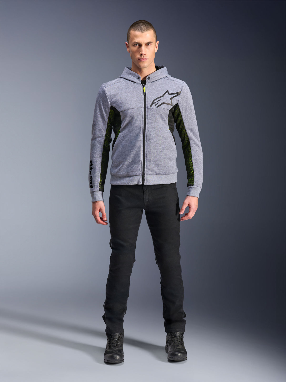 Alpinestars Chrome Air Sport Hoodie, gris chiné et noir, sweat à capuche technique de moto avec panneaux latéraux en mesh noir et accents jaune fluo, logo étoile noir sur la poitrine, porté avec un pantalon et des bottes noirs, style urbain moderne.