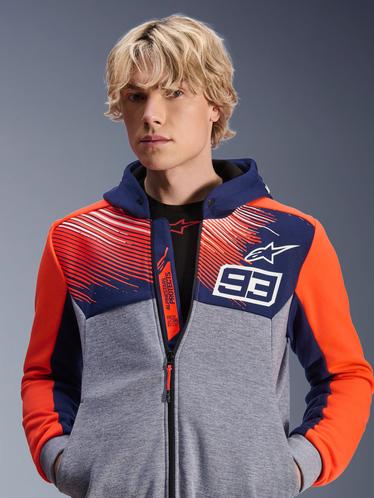 Alpinestars MM93 Chrome V2 Sport Hoodie, sweat à capuche moto urbain, bleu marine et gris chiné avec accents rouge fluo, arborant le marquage Marc Marquez 93 et le logo Alpinestars, design à fermeture éclair intégrale, vêtement lifestyle décontracté pour les motards