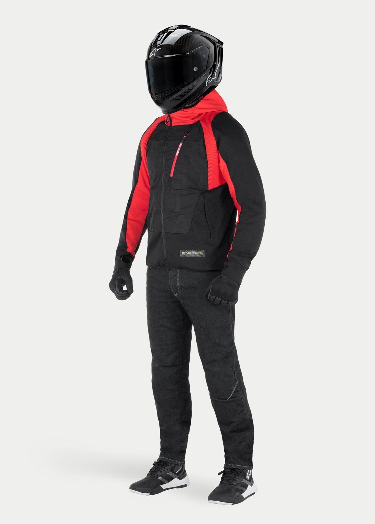 Veste à capuche Alpinestars MO.ST.EQ Hybrid en Noir Rouge Flamme, sweat à capuche de moto urbain avec capuche et détails rouges aux épaules, porté avec un casque intégral noir et un pantalon de moto, design contemporain inspiré du streetwear