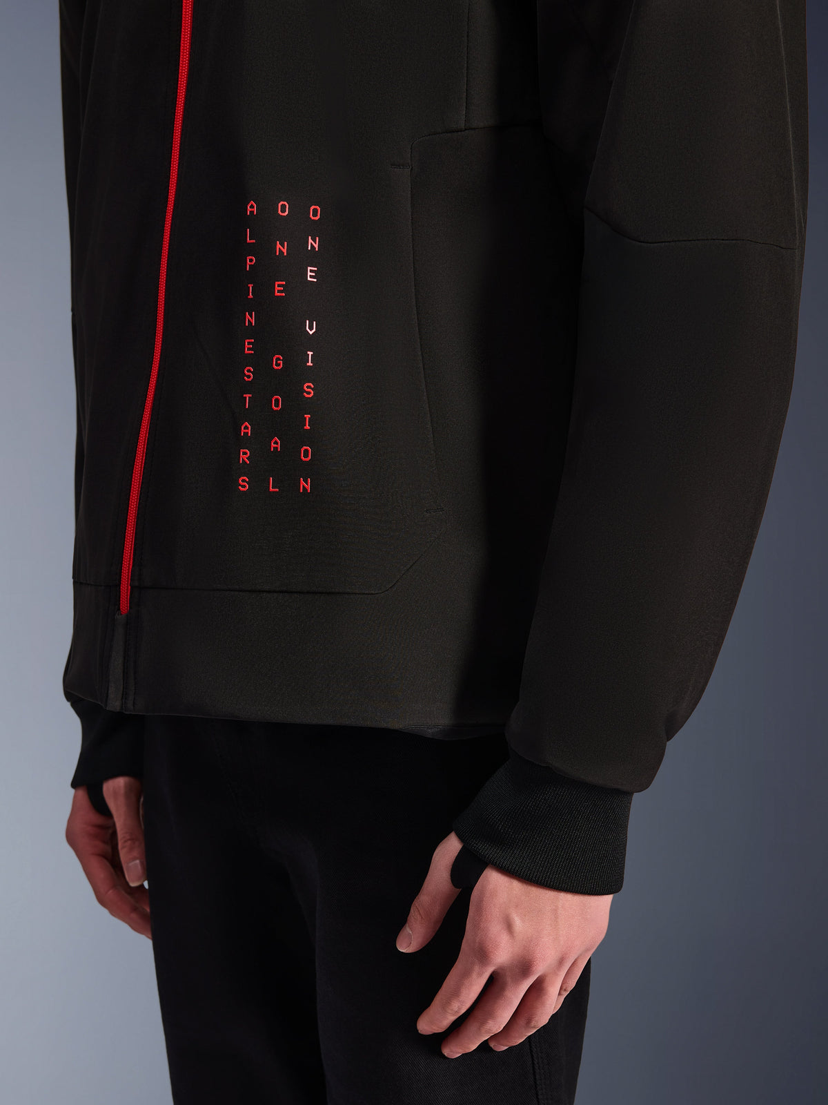 Sweat à capuche Alpinestars Radium Tech, veste de moto urbaine, noir et rouge vif, gros plan sur le graphisme avant avec texte rouge vertical « ALPINESTARS ONE GOAL ONE VISION », fermeture éclair rouge et poignet côtelé avec passe-pouce.