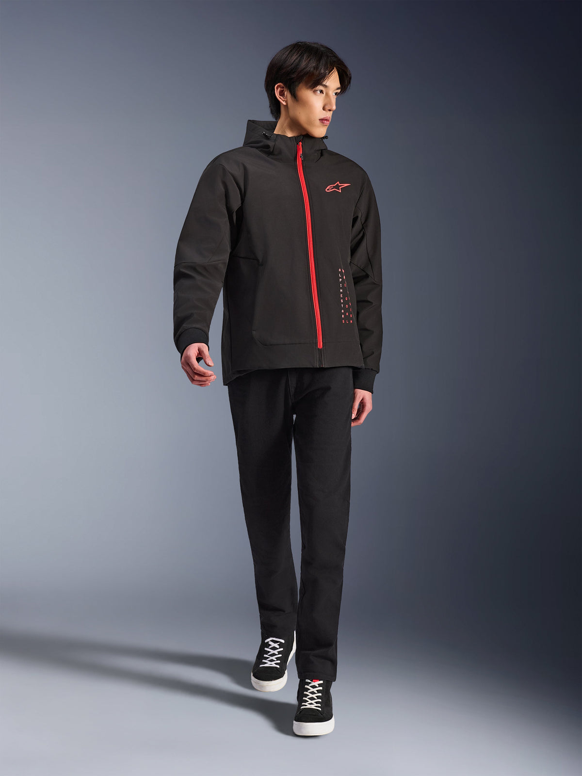 Alpinestars Radium Tech Hoodie en Black Bright Red, veste de moto urbaine portée par un mannequin, dotée d'une fermeture éclair avant rouge et d'un logo sur la poitrine, associée à un pantalon noir et des baskets pour un look urbain moderne.