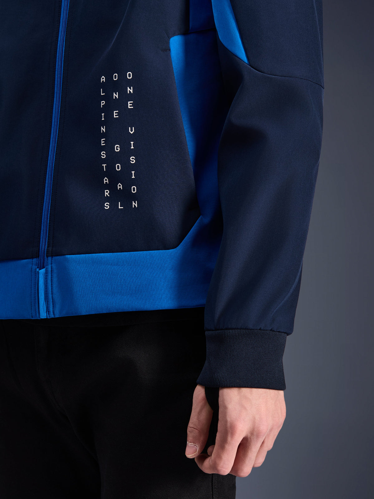 Alpinestars Radium Tech Hoodie, hoodie de moto urbain, bleu marine nuit et bleu royal, gros plan montrant le panneau latéral avec graphisme de texte vertical blanc, poignet extensible côtelé et fermeture à glissière bleue