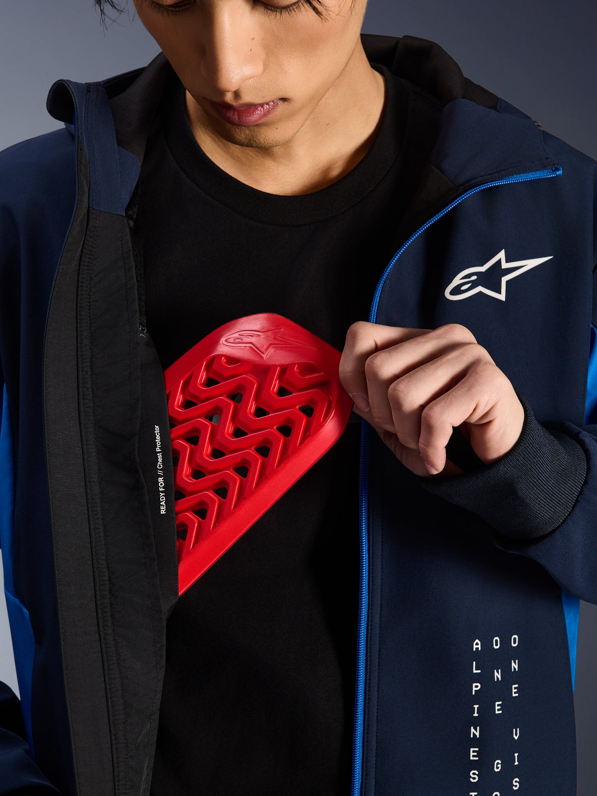 Alpinestars Radium Tech Hoodie en Night Navy et Royal Blue, gros plan montrant une protection pectorale Nucleon rouge insérée dans la poche intérieure, inscription « READY FOR // Chest Protector » sur la doublure et logo étoilé blanc sur la poitrine