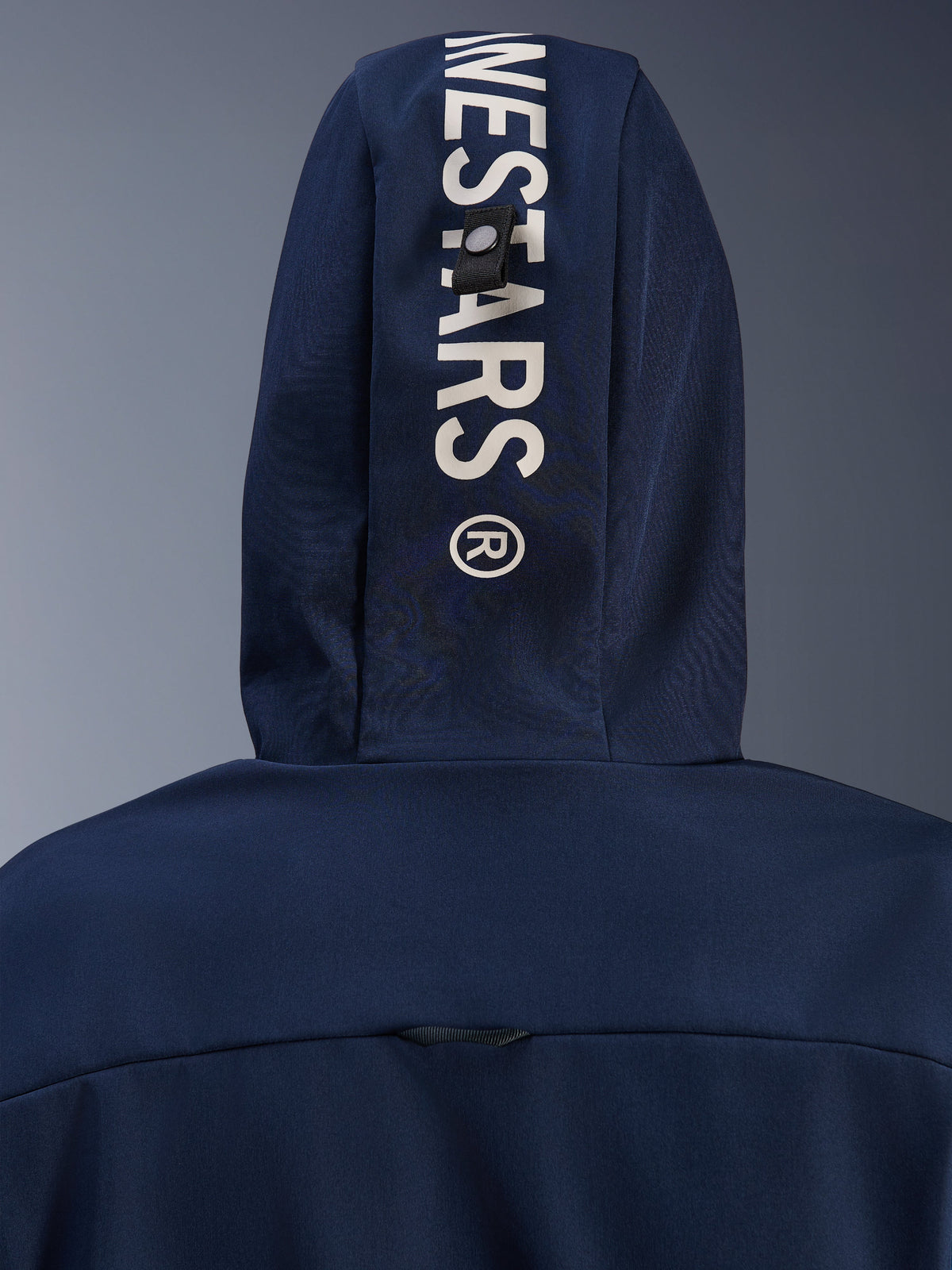 Alpinestars Radium Tech Hoodie en Night Navy Royal Blue, gros plan sur la capuche arrière avec marquage Alpinestars vertical blanc et système de boucle d'attache sécurisée, vêtement technique de moto urbain.