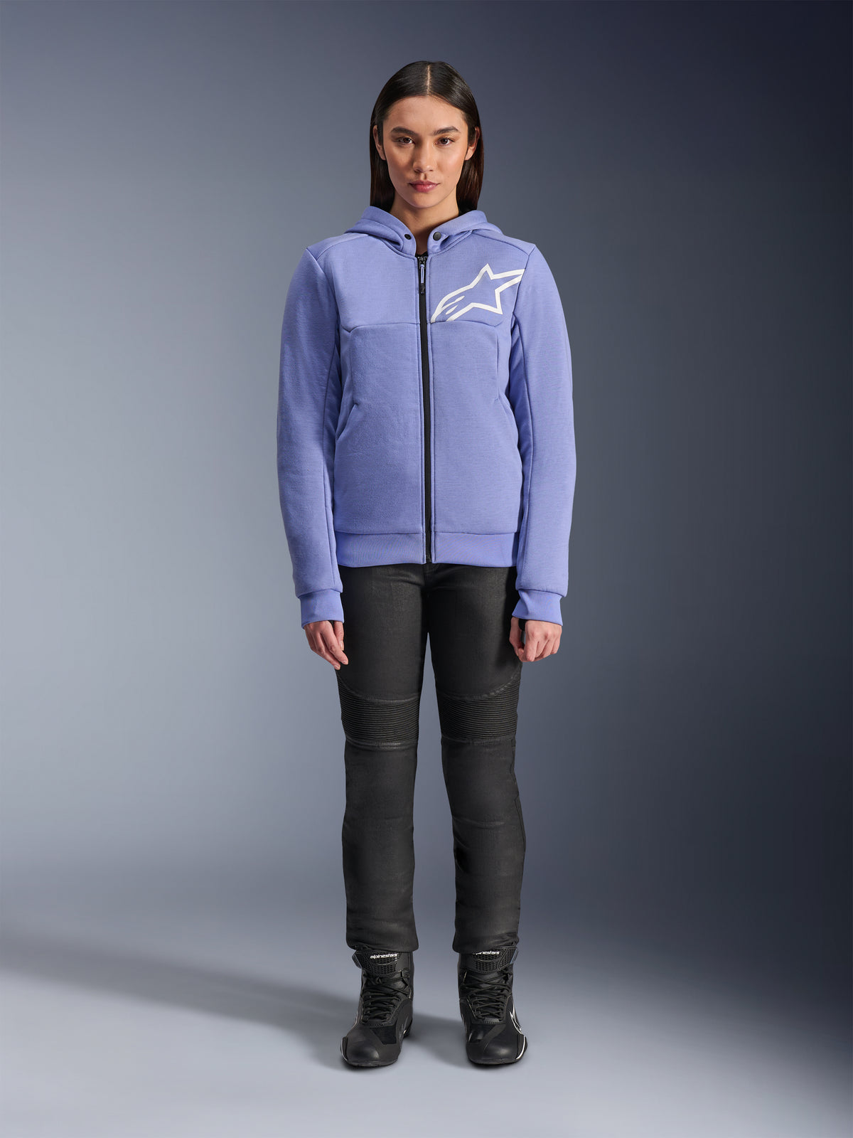 Sweat à capuche Alpinestars Stella Chrome V2 Sport pour femme, bleu violet avec logo Astars blanc sur la poitrine, polaire technique zippée avec capuche, porté avec un pantalon de moto noir et des bottes, équipement de conduite urbaine décontracté pour femme
