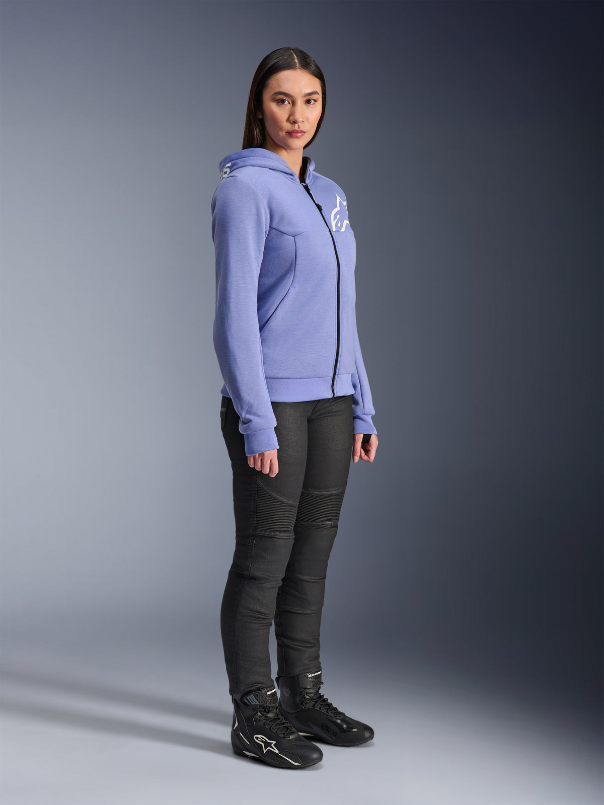 Alpinestars Stella Chrome V2 Sport Hoodie pour femme, sweat à capuche moto bleu-violet avec logo Alpinestars blanc sur la poitrine, porté par un mannequin avec un pantalon de moto noir et des bottes de moto noires, vêtement de conduite urbaine pour femme