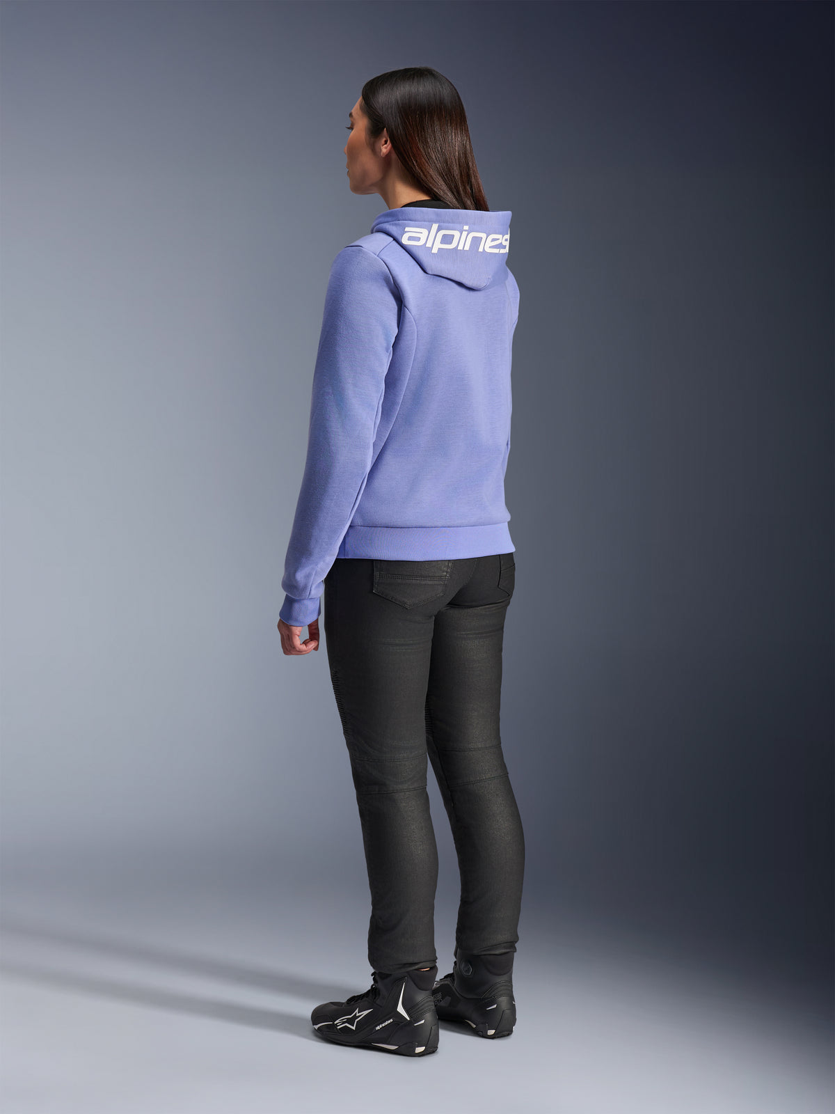 Alpinestars Stella Chrome V2 Sport Hoodie pour femme, bleu violet, vue arrière montrant le marquage blanc sur la capuche, porté avec un pantalon de moto noir et des bottes de moto noires, équipement de moto urbain décontracté