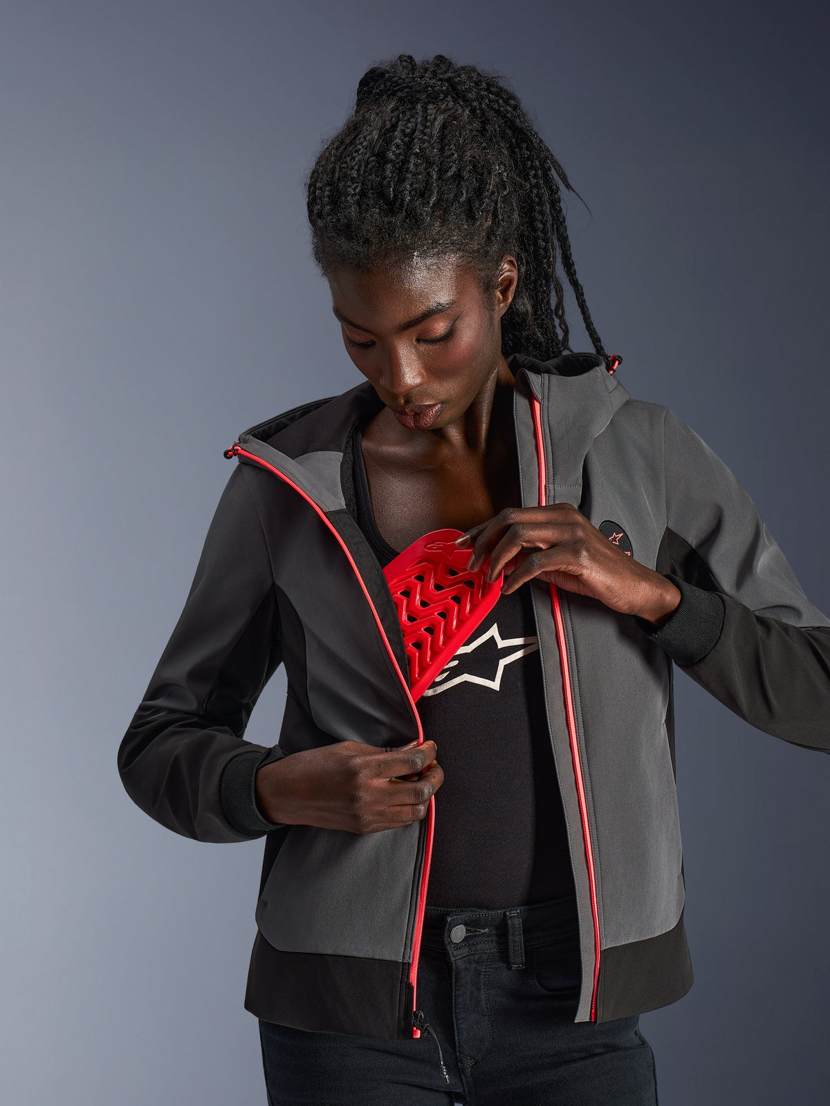 Alpinestars Stella Radium Tech Hoodie pour femme, gris foncé et noir, mannequin présentant la protection amovible rouge Nucleon Flex Plus, sweat à capuche de moto urbain avec accents de fermeture éclair roses