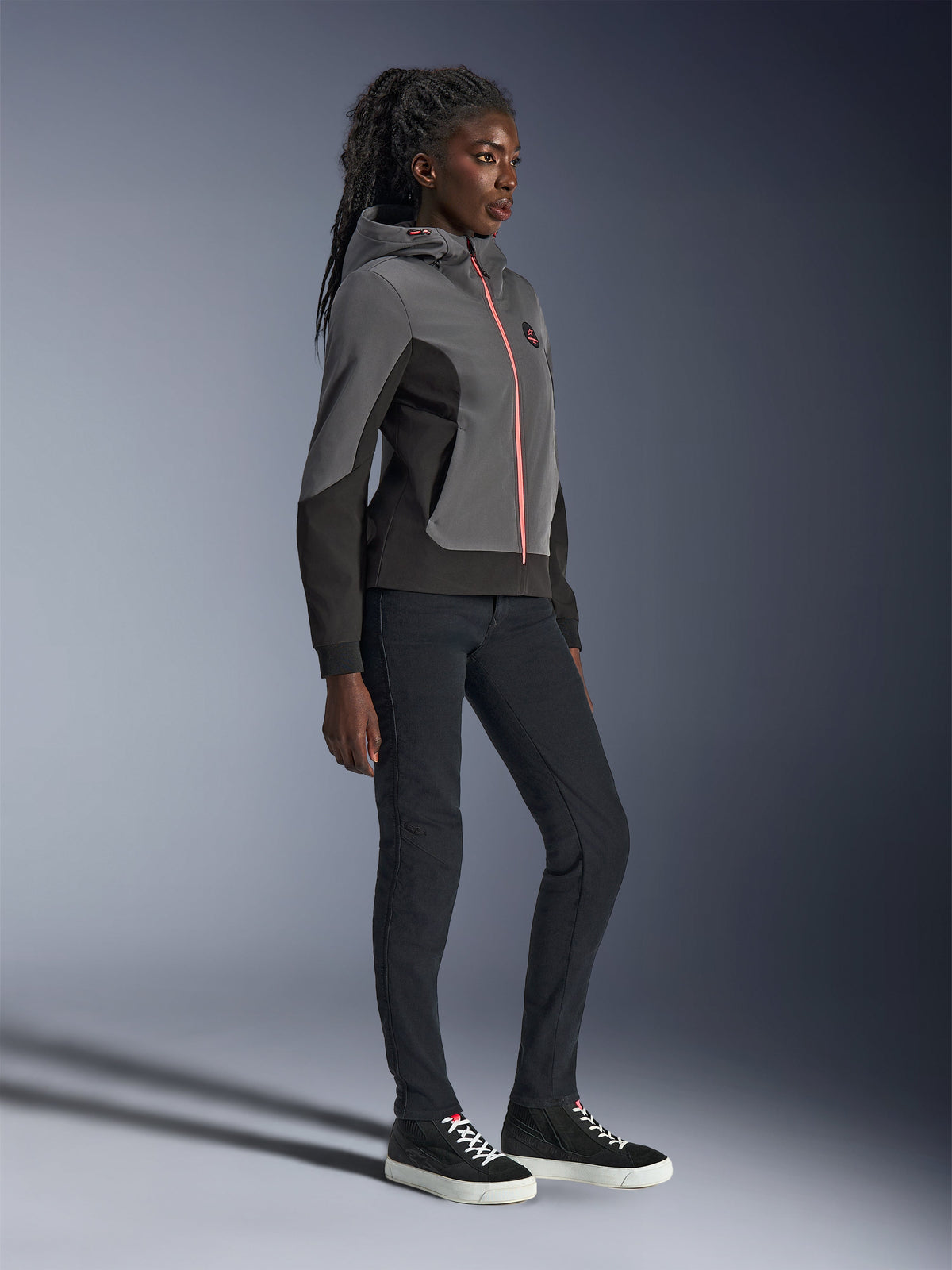 Alpinestars Stella Radium Tech Hoodie, sweat à capuche de moto urbain, gris foncé et noir avec fermeture éclair orange vif, porté avec un pantalon noir et des baskets noires, coupe athlétique spécifique aux femmes