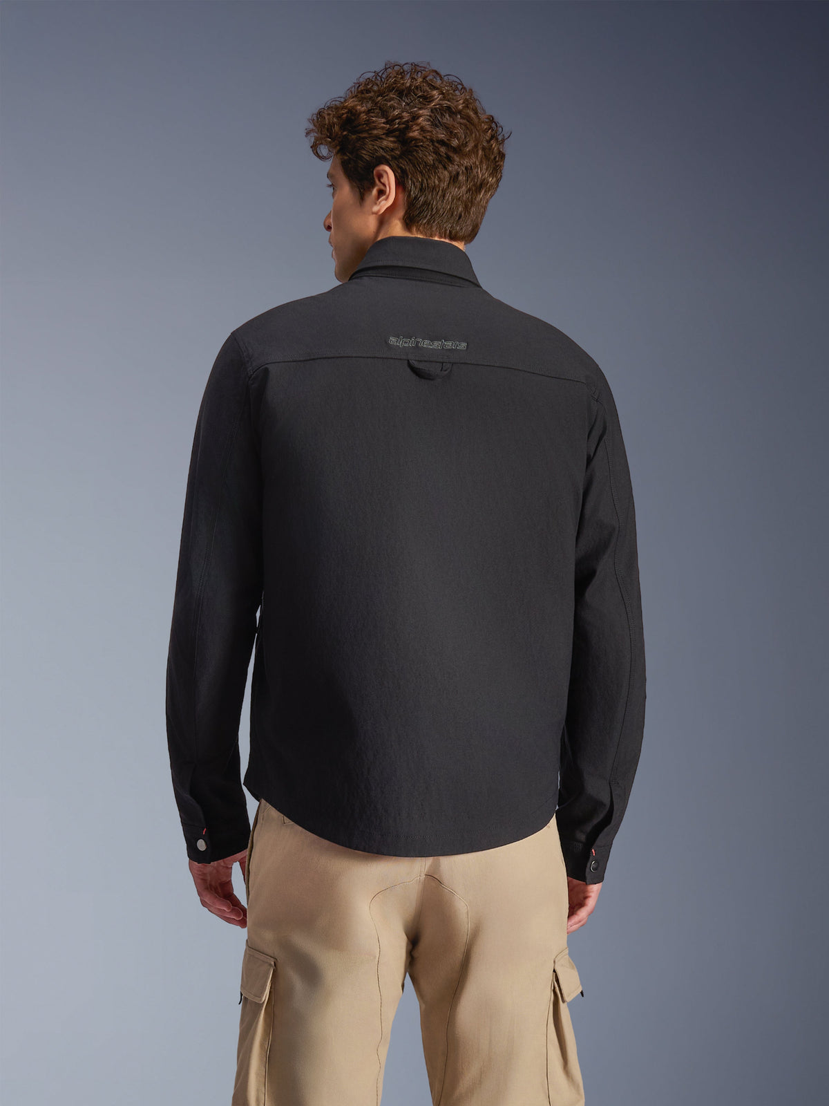 Alpinestars Bryon Water Resistant Overshirt, Black, Rear view worn by model, featuring embroidered branding on the back yoke and utility hanging loop, styled with tan cargo pants, urban motorcycle gear with classic workwear aesthetic
