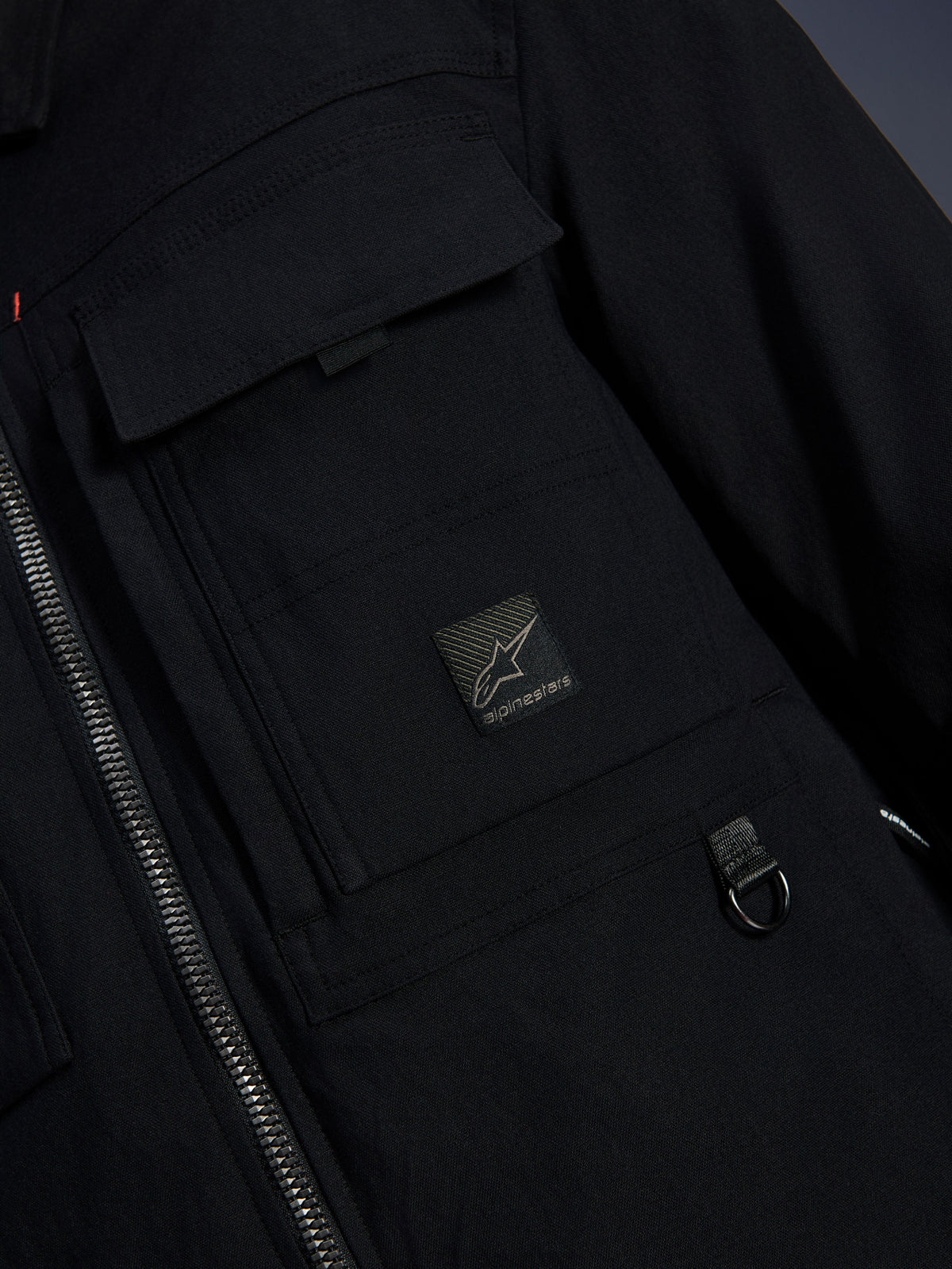 Alpinestars Bryon Water Resistant Overshirt, Black, close-up view of waxed canvas fabric, front zipper, chest cargo pocket with Alpinestars logo patch, and metal D-ring detail