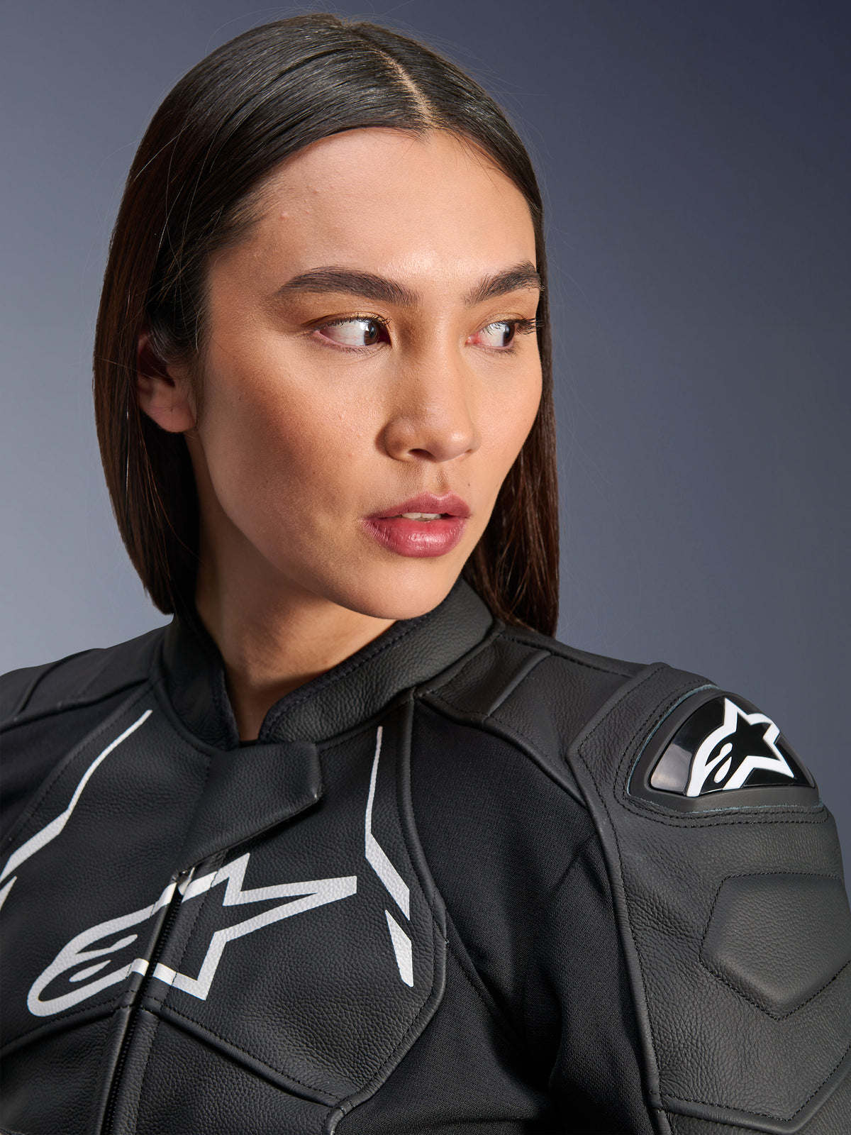 Femme portant la veste en cuir Alpinestars Stella Dusk en Noir et Blanc, portrait en gros-plan présentant le logo Alpinestars blanc sur la poitrine et la protection d'épaule externe DFS, construction en cuir de qualité supérieure pour la course moto sur route