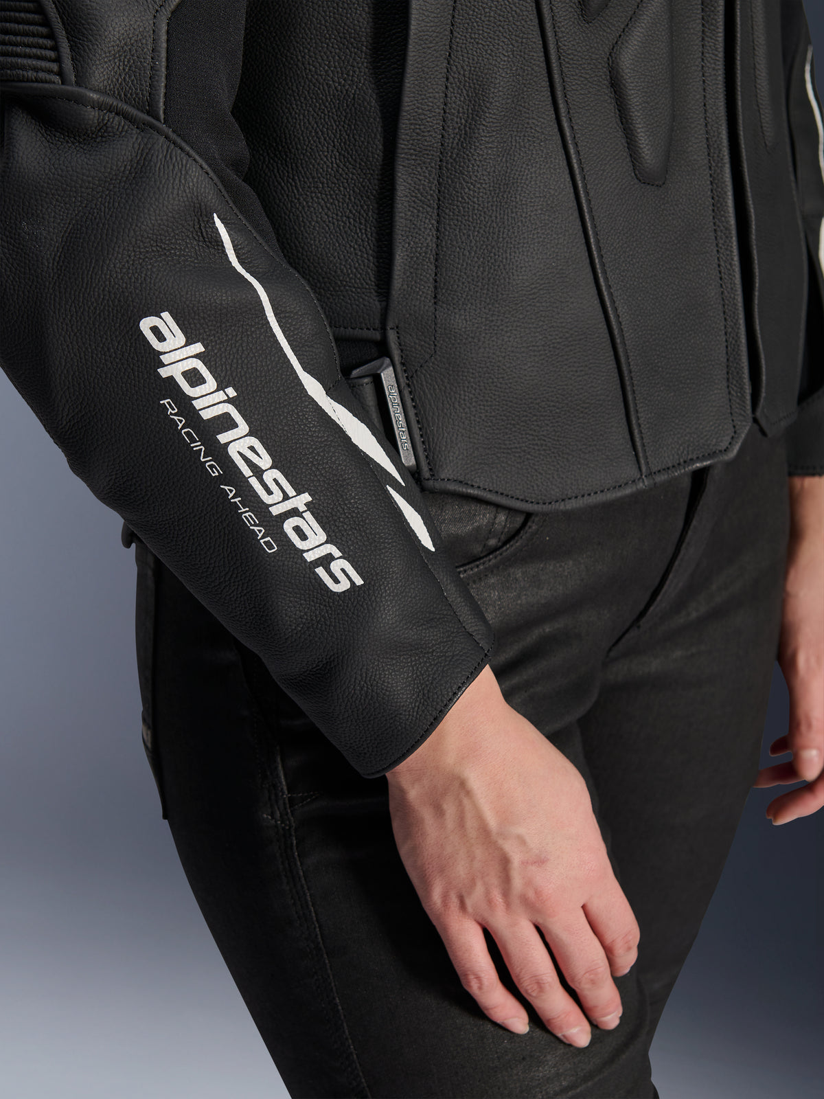 Gros plan sur la veste en cuir Alpinestars Stella Dusk, veste de moto en cuir noir pour femme, avec logo blanc 'alpinestars RACING AHEAD' sur la manche, texture en cuir bovin premium, portée avec un pantalon noir