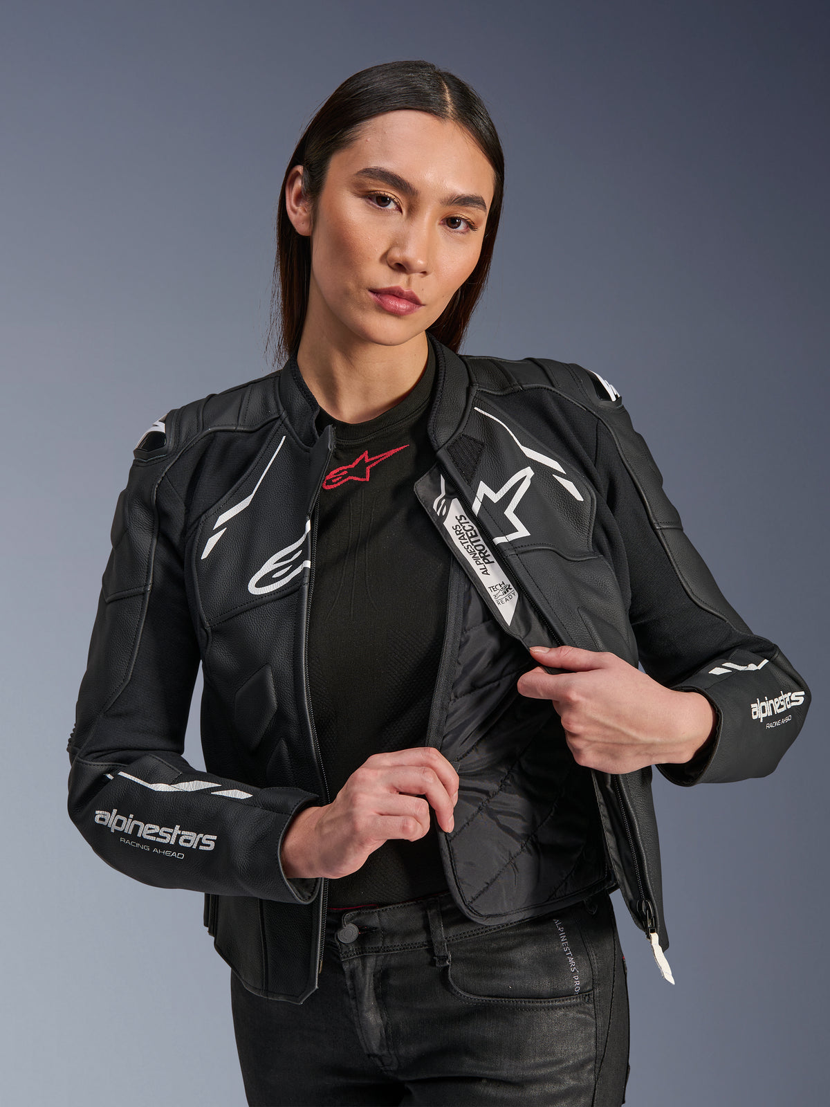 Mannequin femme portant la veste en cuir Alpinestars Stella Dusk Noir et Blanc, présentant la doublure thermique matelassée interne et l'étiquette Tech-Air Ready, cuir bovin premium avec logo étoile blanc et marquage 'RACING AHEAD' sur la manche