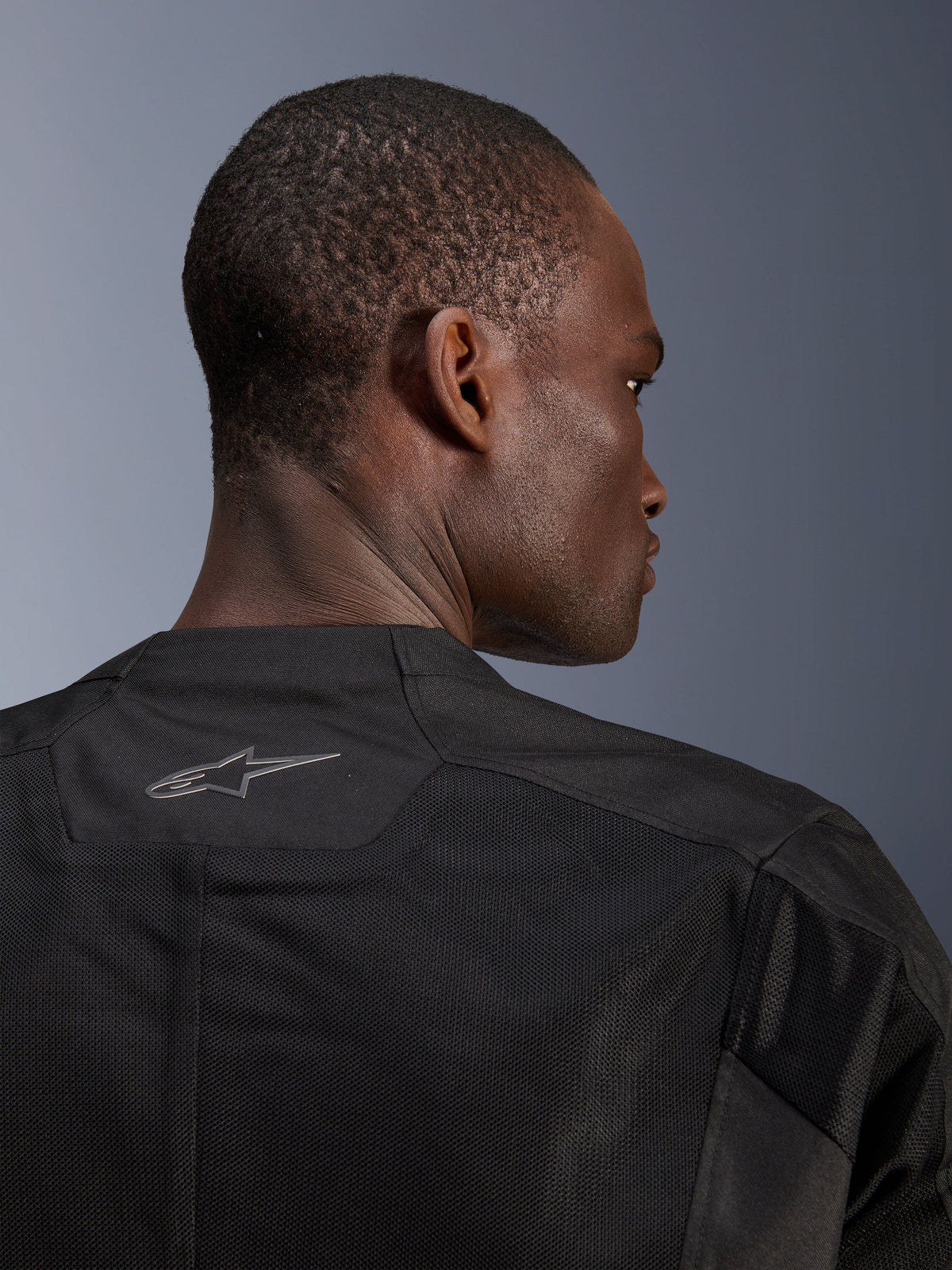 Veste Alpinestars C-1 Air, veste de moto noire, gros plan de l'arrière montrant les panneaux en maille technique respirante et le logo Alpinestars réfléchissant sur le col, équipement de conduite urbaine
