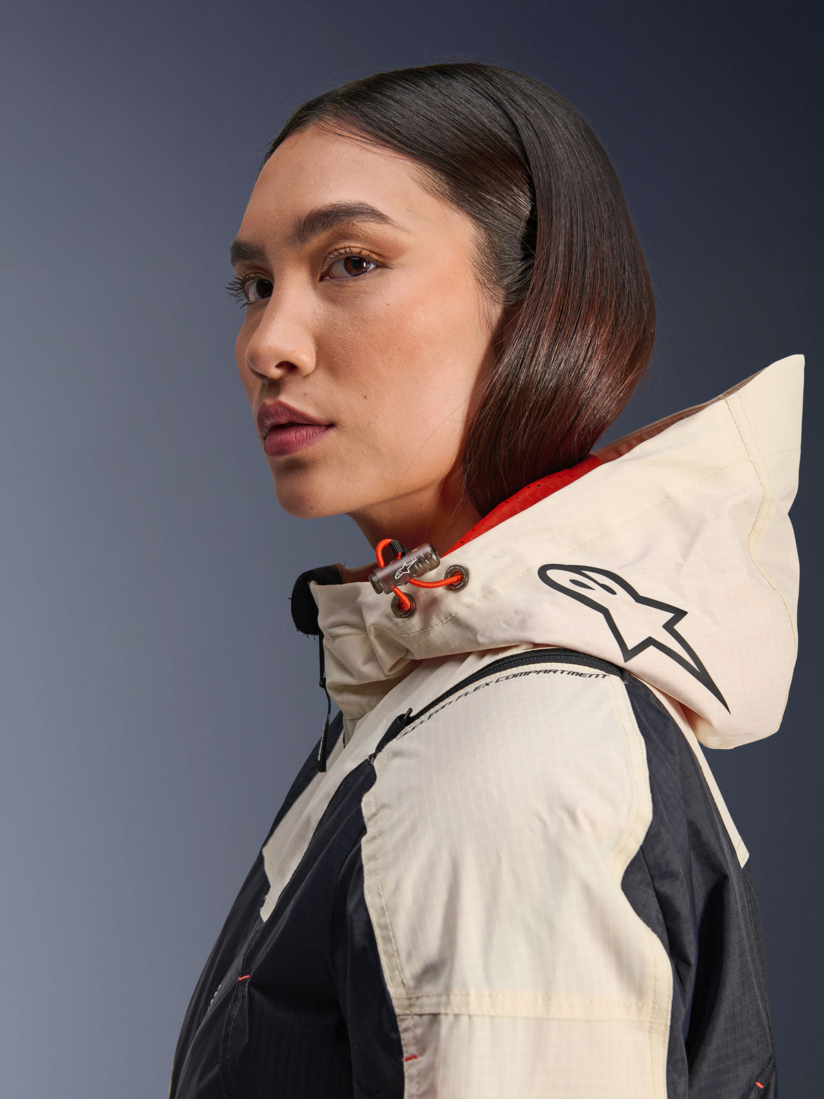 Veste Alpinestars Molly Air, Black Almond, veste de moto urbaine contemporaine, vue de profil d'un modèle portant la capuche avec le logo Alpinestars et des accents de cordon orange, texture en tissu ripstop