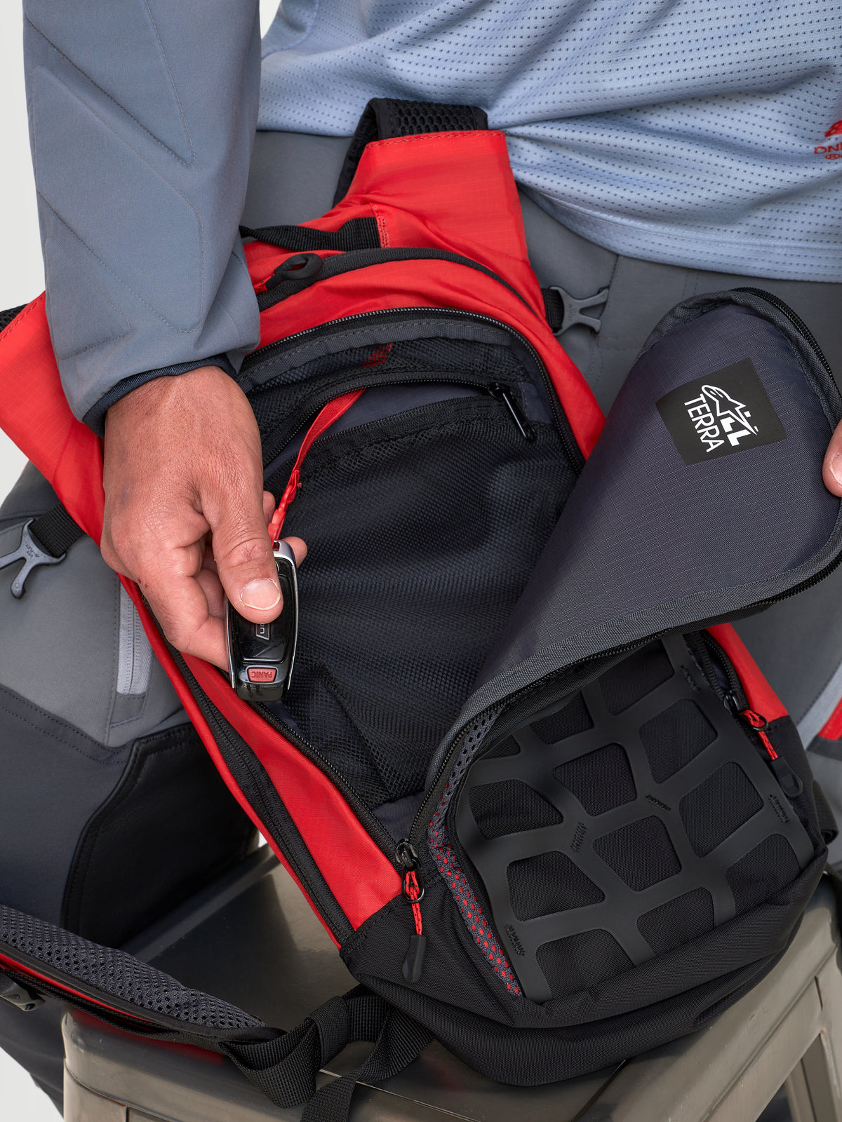 Alpinestars Sac À Dos AT-9, sac à dos de moto MX rouge et noir, vue rapprochée montrant les compartiments de rangement organisés et la fermeture zippée lors de l'utilisation par un modèle