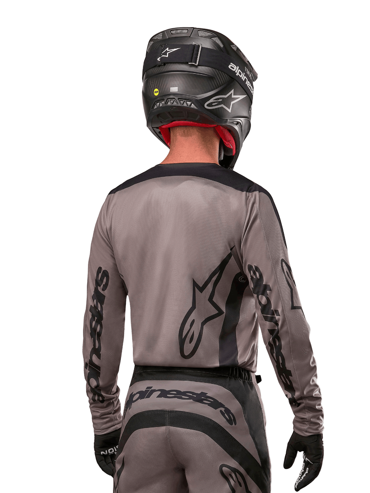 Pilote de motocross vu de dos portant le maillot Alpinestars Fluid Lurv 2024 en Mud Black, avec logo Alpinestars noir sur les manches et le dos, associé à un casque noir et un équipement assorti pour la course tout-terrain