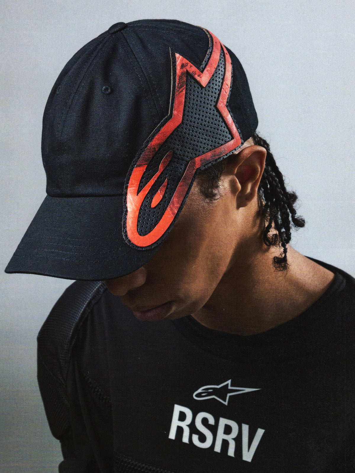 Alpinestars RSRV Lowside Hat, casquette noire avec design flamme rouge et noir, logo RSRV visible sur le t-shirt, style streetwear premium