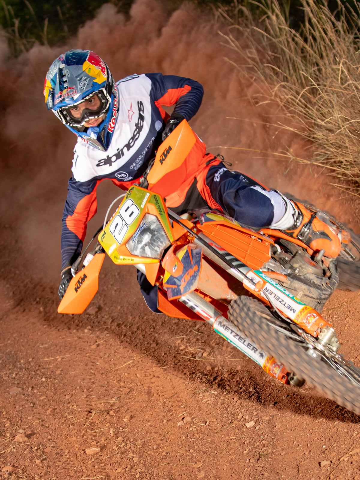 Pilote d'enduro en action sur une moto tout-terrain orange, portant le maillot Alpinestars Pro-Dura en bleu marine, orange vif et blanc, offrant une conception légère et respirante avec un marquage distinctif pour la performance tout-terrain.