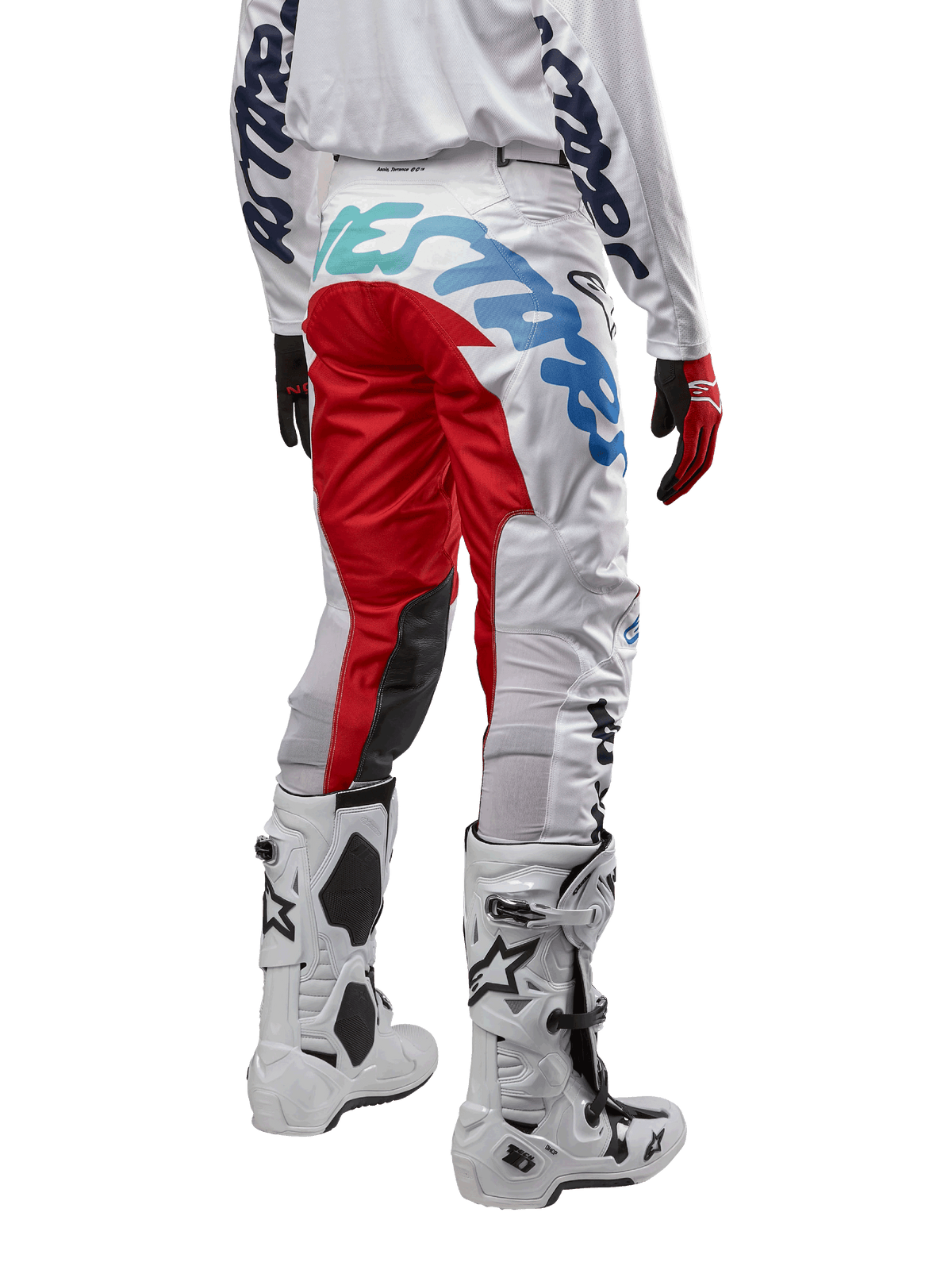 Alpinestars Racer Hana Pants 2024, pantalon de motocross, blanc multicolore avec des accents rouges et bleus, vue arrière montrant un marquage important sur l'assise, porté avec des bottes de motocross blanches et noires, conçu pour la performance et la durabilité en tout-terrain