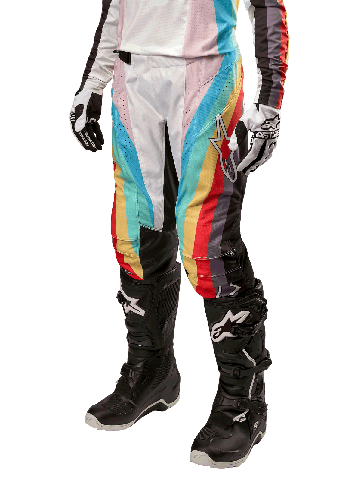 Alpinestars Stella Techstar 2024, pantalon de motocross pour femme, noir multicolore avec rayures diagonales rouges, jaunes et bleues, porté avec des bottes de moto noires et des gants blancs, avec panneaux de protection noirs aux genoux et marquage audacieux pour la course tout-terrain