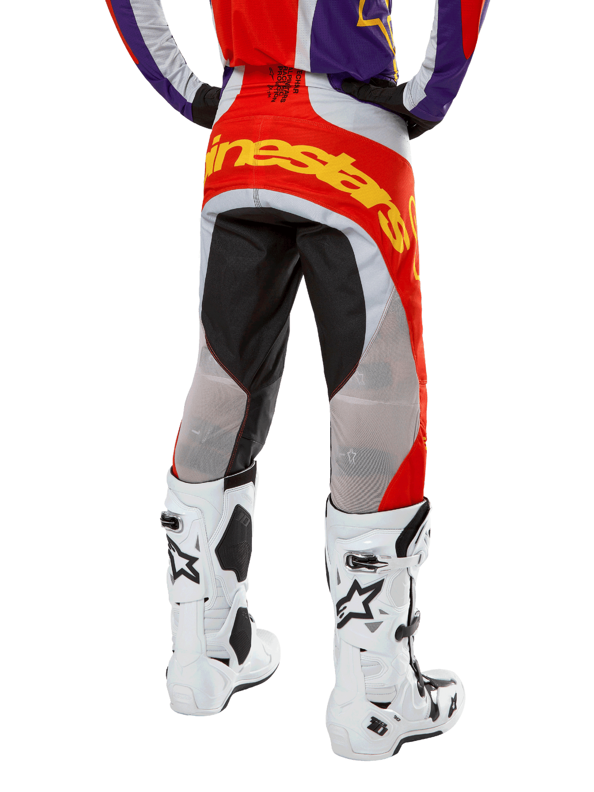 Pantalon Alpinestars Techstar Ocuri 2024, pantalon de motocross, orange vif, violet et noir, vue arrière de la taille vers le bas, marquage jaune vif sur l'assise, empiècements techniques noirs et gris, associé à des bottes de motocross blanches.