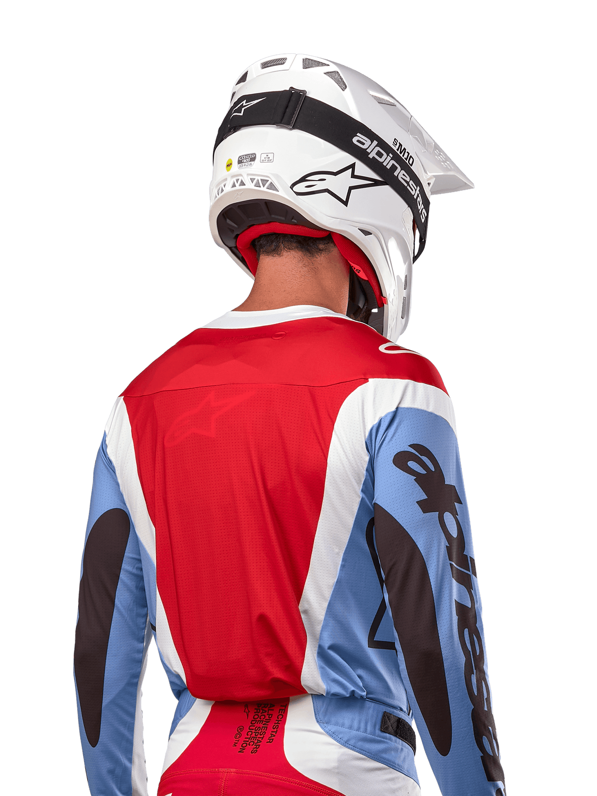 Alpinestars Maillot Techstar Ocuri 2024, maillot de motocross, bleu clair, rouge Mars et blanc, vue arrière d'un pilote portant un casque blanc assorti et des lunettes noires, avec marquage noir audacieux sur les manches et coupe ergonomique pour la performance tout-terrain