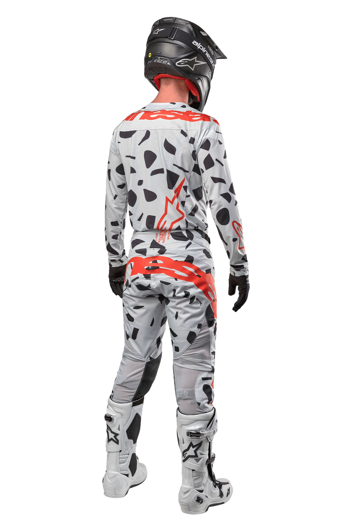 Pilote de motocross vu de dos portant le pantalon Alpinestars Techstar Rantera 2024, camouflage gris avec taches noires et logos rouges, maillot assorti, casque noir et bottes blanches, tenue de course tout-terrain complète