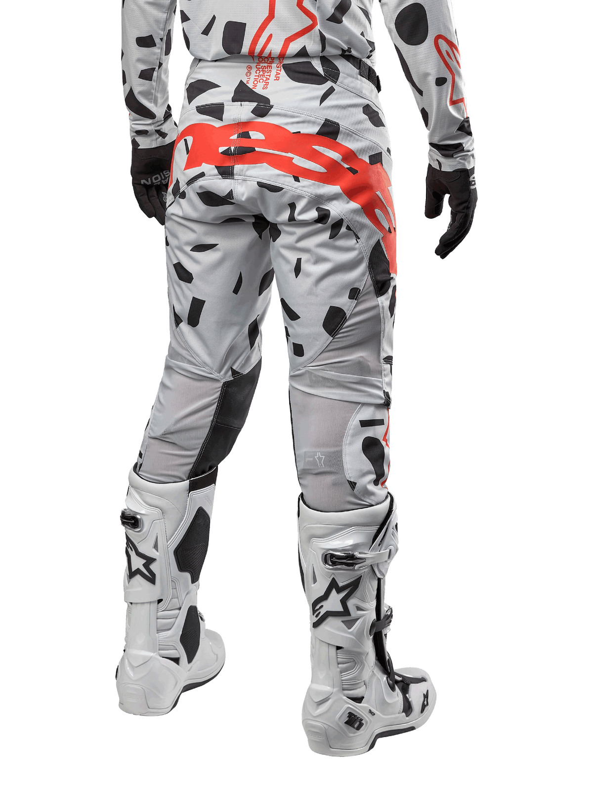 Pantalon Alpinestars Techstar Rantera 2024, pantalon de motocross, Haze Gray Camo avec motifs de camouflage noirs et un grand logo Alpinestars rouge sur l'assise, vue arrière porté avec des bottes blanches et un équipement de course assorti