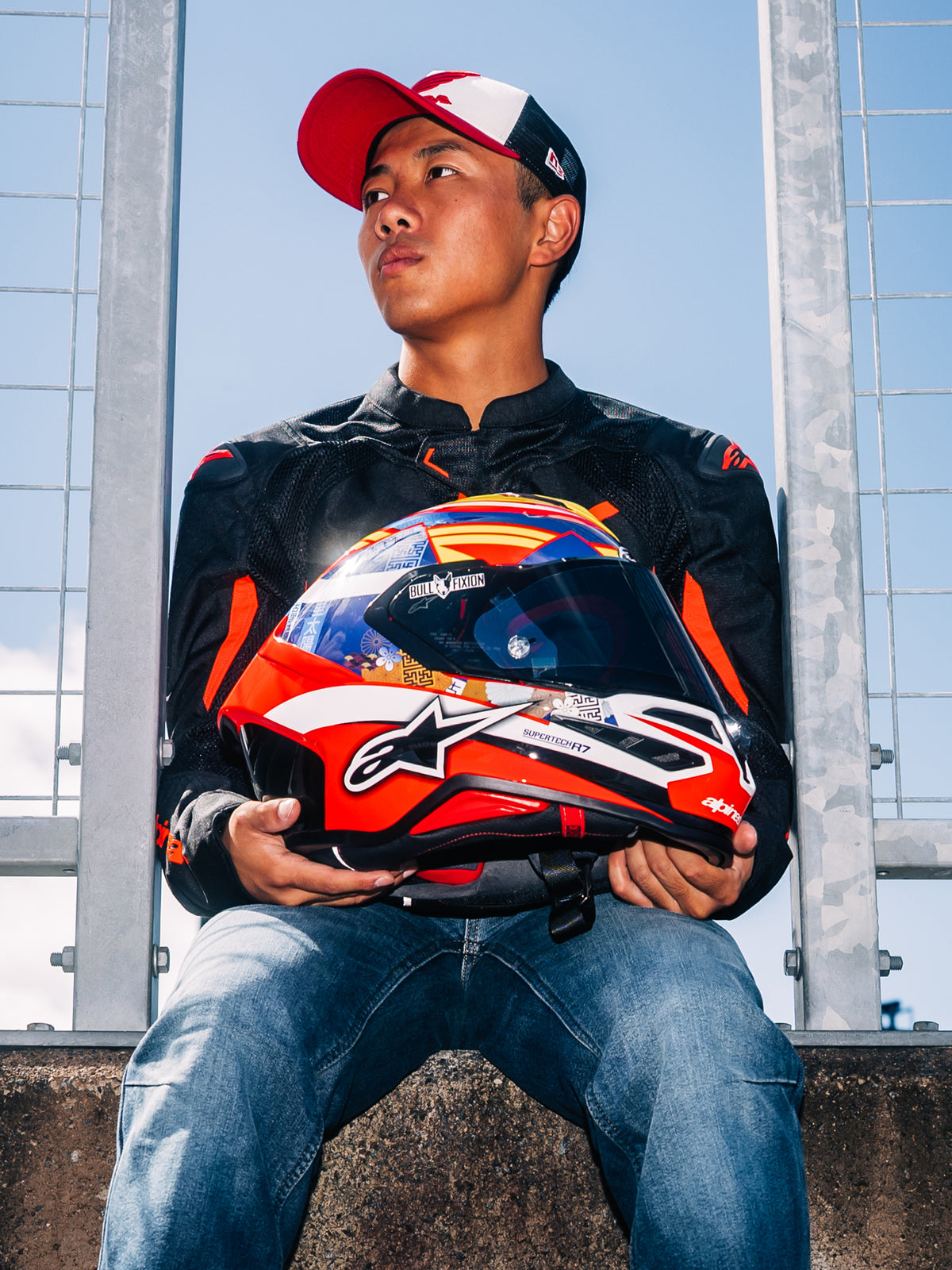 Casque Alpinestars S-R7 Taiyo Furusato, casque de moto intégral racing, graphisme rouge, blanc et bleu, tenu par le pilote Taiyo Furusato portant une veste noire, vue extérieure en bord de piste