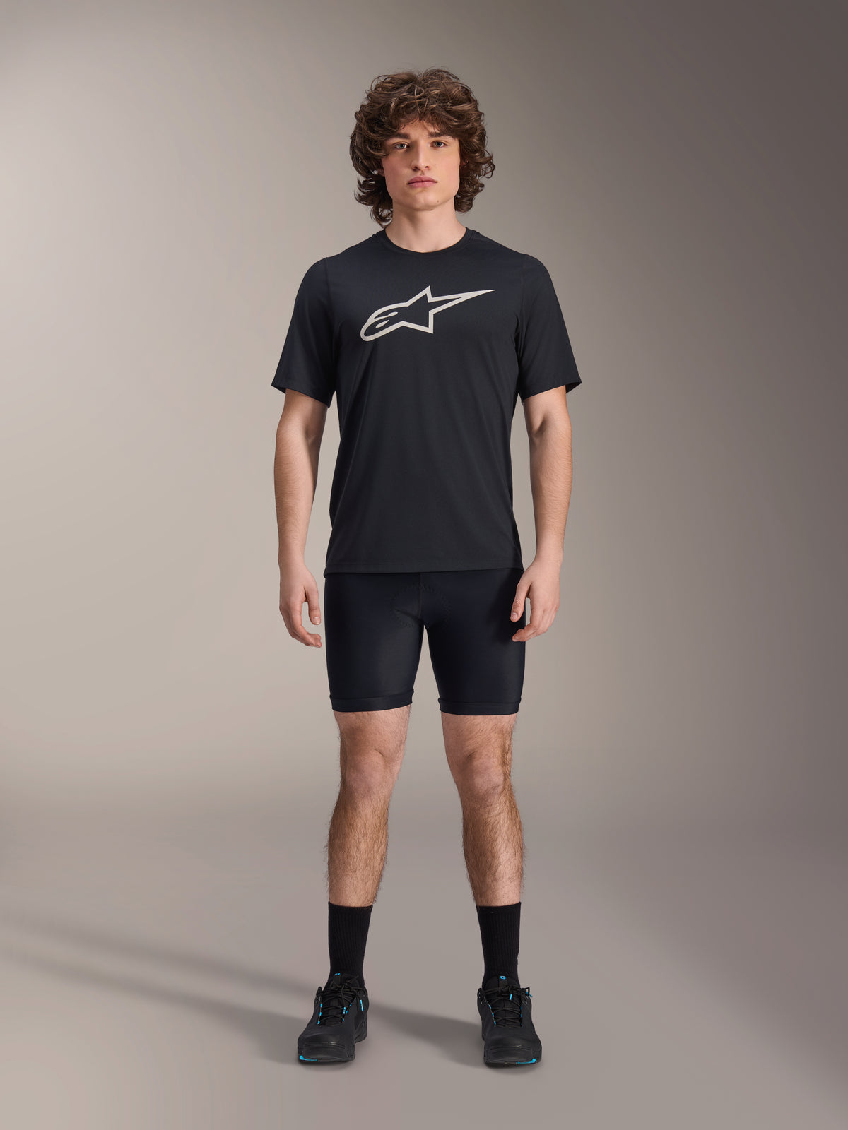 Short Liner Alpinestars A-Dura, sous-short de cyclisme noir, porté par un mannequin avec un t-shirt noir à logo Alpinestars et des chaussures de cyclisme noires, coupe ajustée pour la performance en VTT et le confort en selle