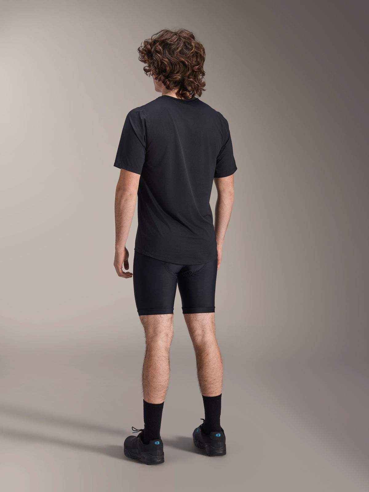 Alpinestars A-Dura Liner Shorts, short de cyclisme noir, vue de dos sur modèle, tissu extensible ajusté avec coutures de rembourrage de chamois visibles, associé à un t-shirt noir et des chaussures de cyclisme, équipement de VTT