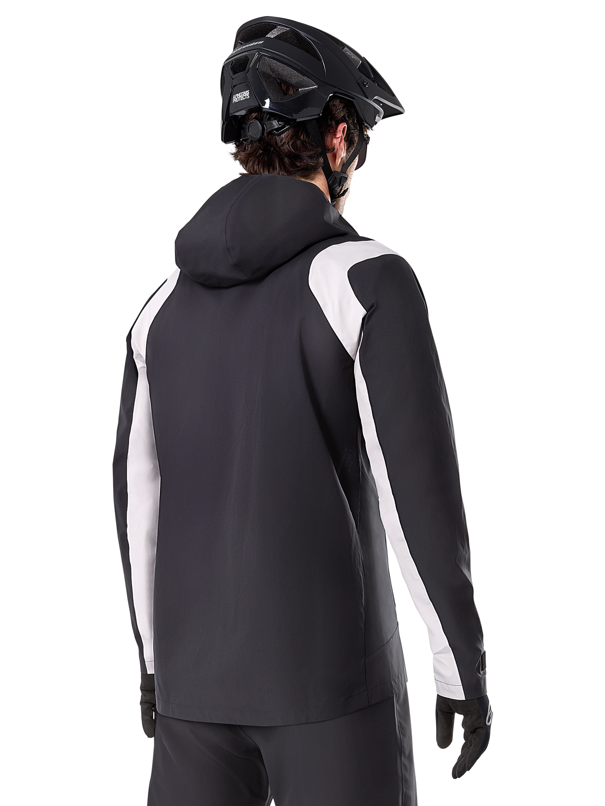 Veste de pluie Alpinestars A-Dura, veste de pluie pour VTT, noire avec empiècements blancs sur les manches, vue arrière d'un cycliste portant un casque de VTT noir et des gants, construction technique imperméable à 2,5 couches, équipement de VTT