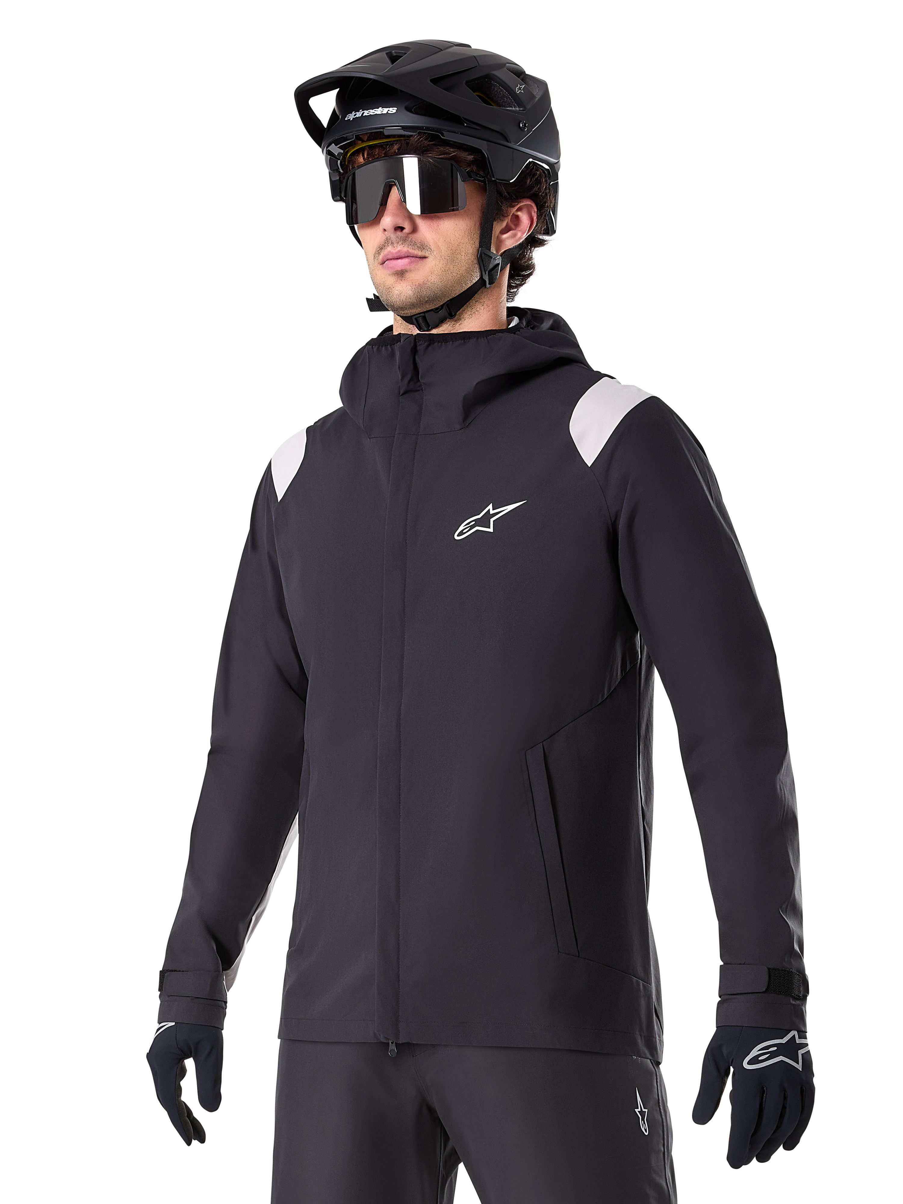 Veste de pluie Alpinestars A-Dura, veste de pluie pour VTT, noire avec accents gris clair sur les épaules, portée par un cycliste avec un casque de VTT noir et des lunettes de soleil, logo blanc sur la poitrine, construction imperméable, coordonnée avec un pantalon et des gants noirs pour le cyclisme tout-terrain