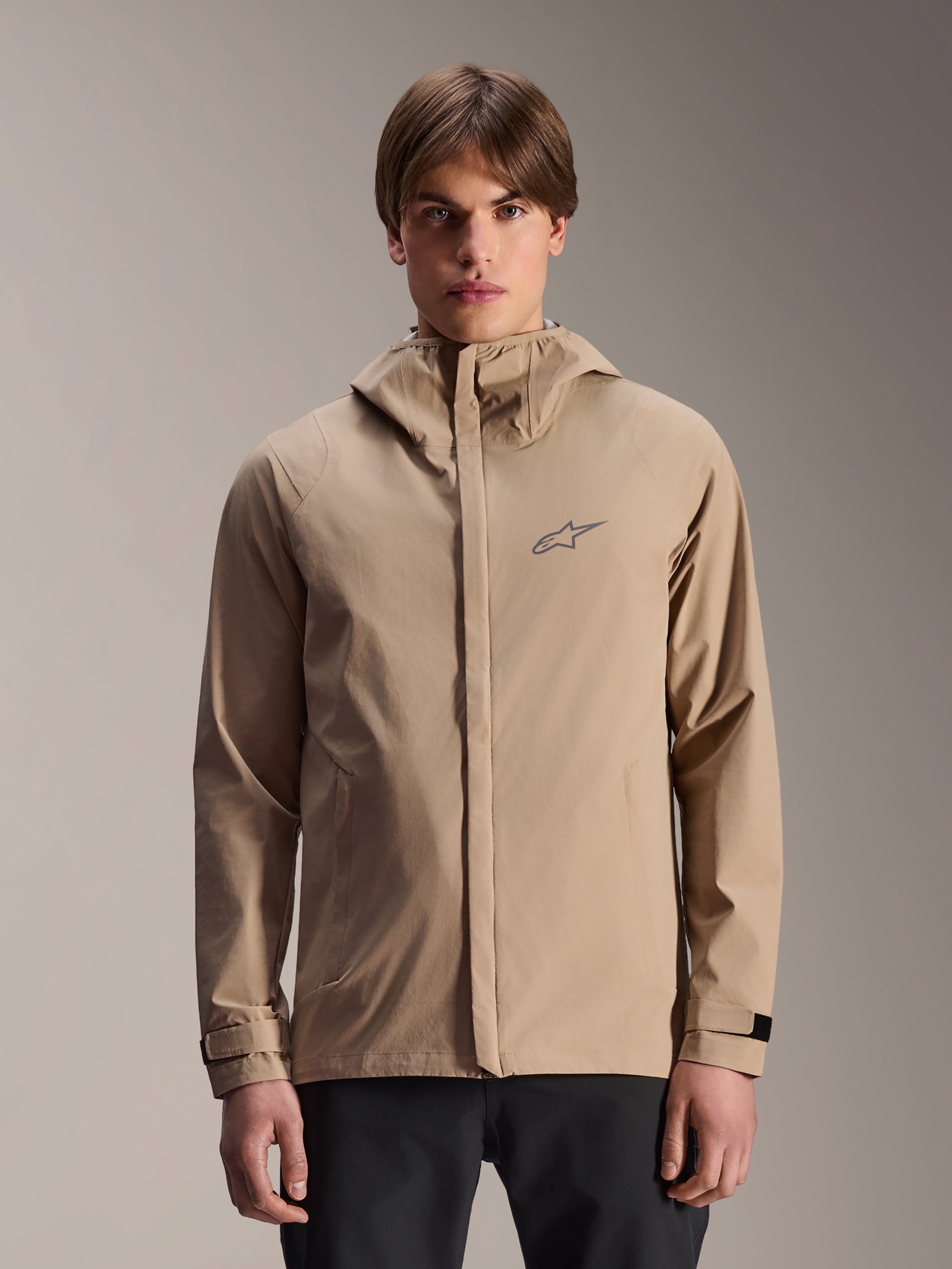Alpinestars A-Dura Rain Jacket, Light Brown hooded mountain bike rain jacket, worn by a model, featuring a small chest logo, adjustable cuff straps, and concealed front zipper, waterproof cycling gear