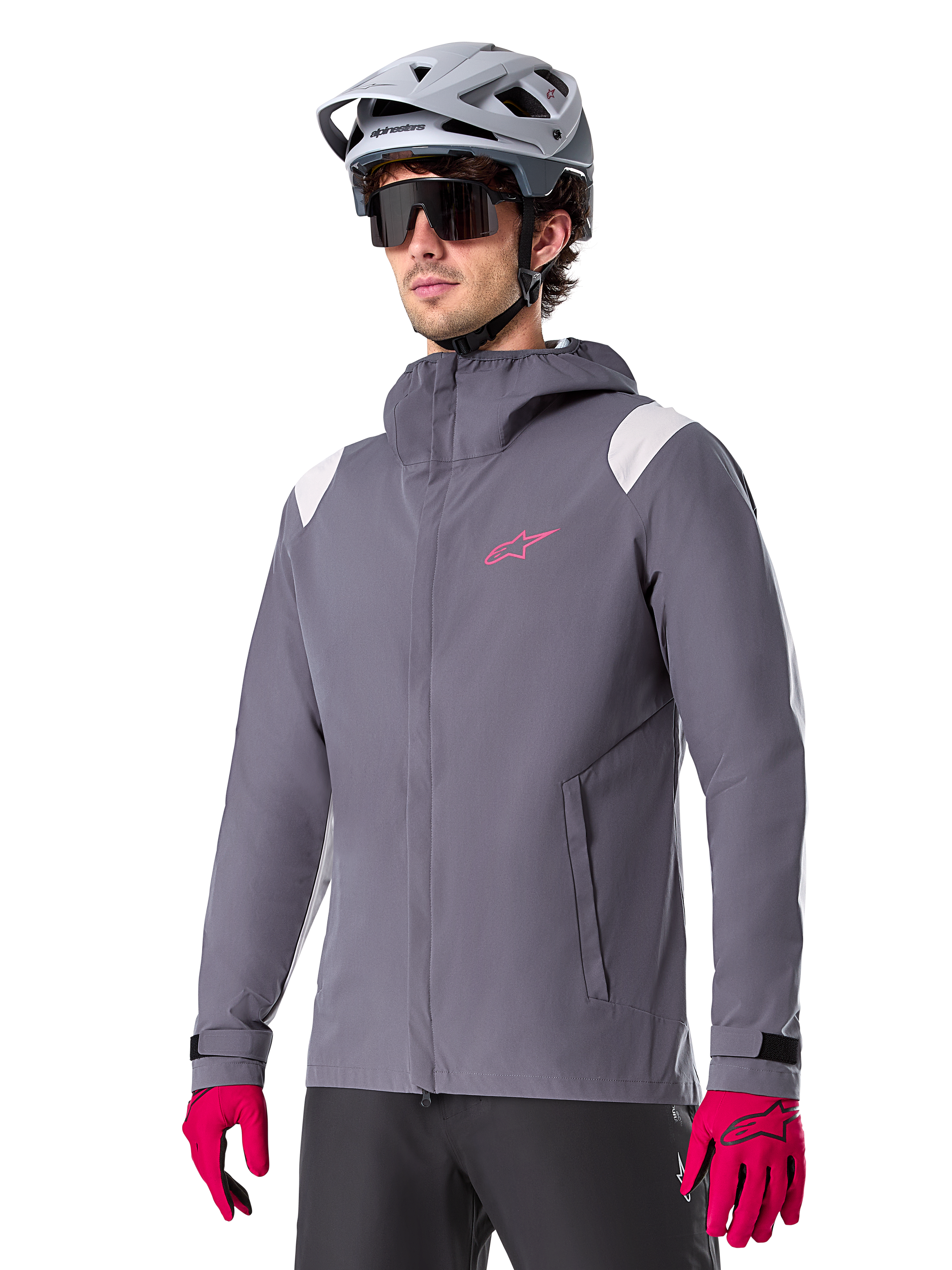 Veste de pluie Alpinestars A-Dura, veste de pluie pour VTT, gris titane foncé avec logo rose et accents blancs sur les épaules, modèle à capuche avec poches avant, portée avec des gants roses et un casque de vélo gris clair