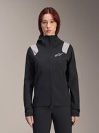 Alpinestars Stella A-Dura Rain Jacket, veste de pluie de cyclisme pour femme, noire avec empiècements gris clair sur les épaules, veste technique à capuche avec logo blanc sur la poitrine, poignets réglables par Velcro, équipement professionnel pour le VTT et le cyclisme par temps humide
