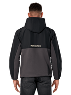 Veste hybride Juncture Alpinestars, vue de dos, noir et gunmetal, anorak sportswear décontracté avec construction en matériaux mixtes, partie supérieure en ripstop et partie inférieure en polaire de toile, logo Alpinestars au dos, porté avec un pantalon sombre