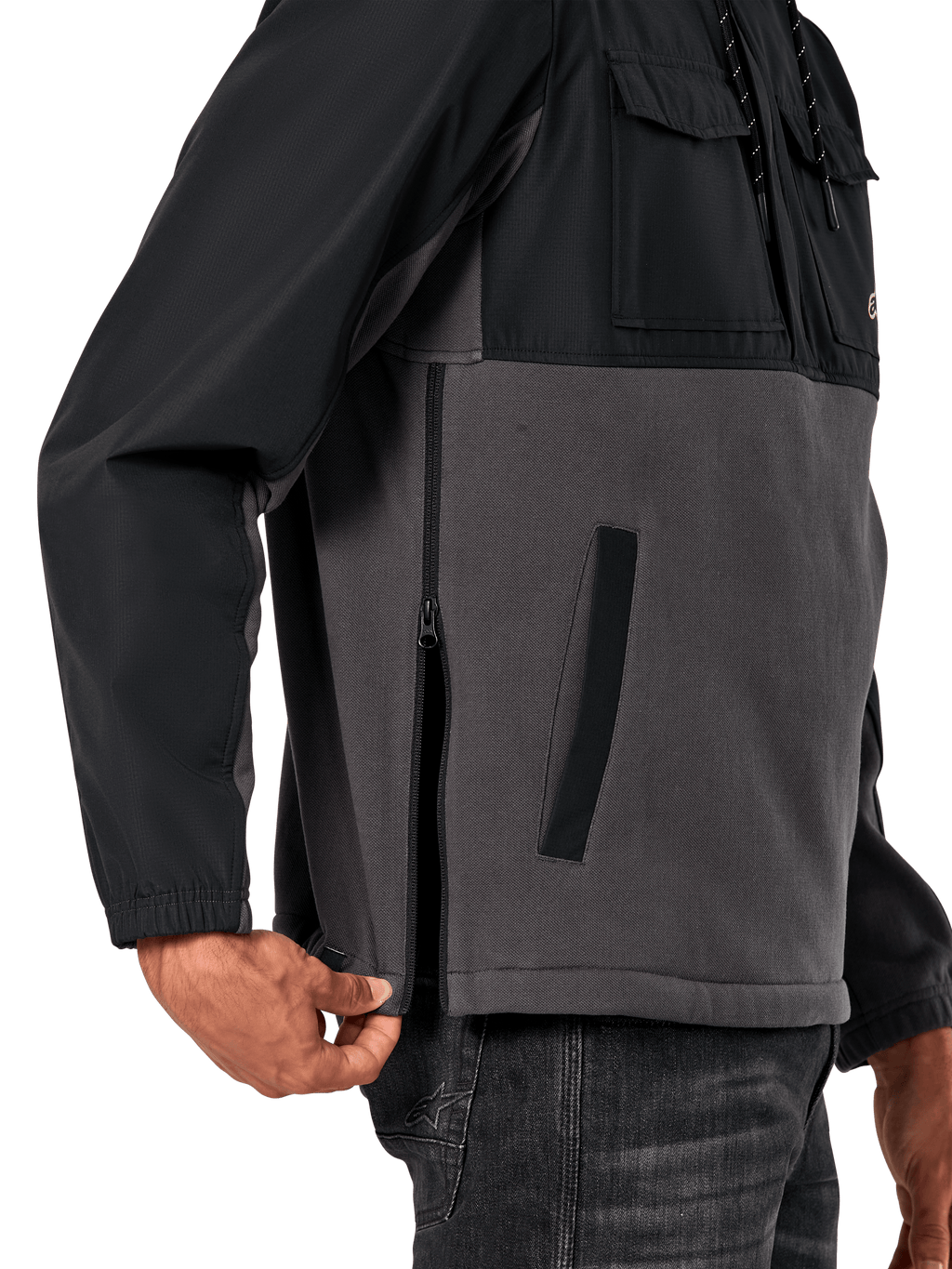 Veste Hybride Juncture Alpinestars en Noir Gunmetal, vue latérale détaillée mettant en évidence la fermeture éclair latérale et la poche passepoilée inférieure, conception multi-matières avec polaire de toile grise et empiècements ripstop noirs, streetwear décontracté inspiré du sport automobile