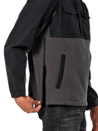 Veste Hybride Juncture Alpinestars en Noir Gunmetal, vue latérale détaillée mettant en évidence la fermeture éclair latérale et la poche passepoilée inférieure, conception multi-matières avec polaire de toile grise et empiècements ripstop noirs, streetwear décontracté inspiré du sport automobile