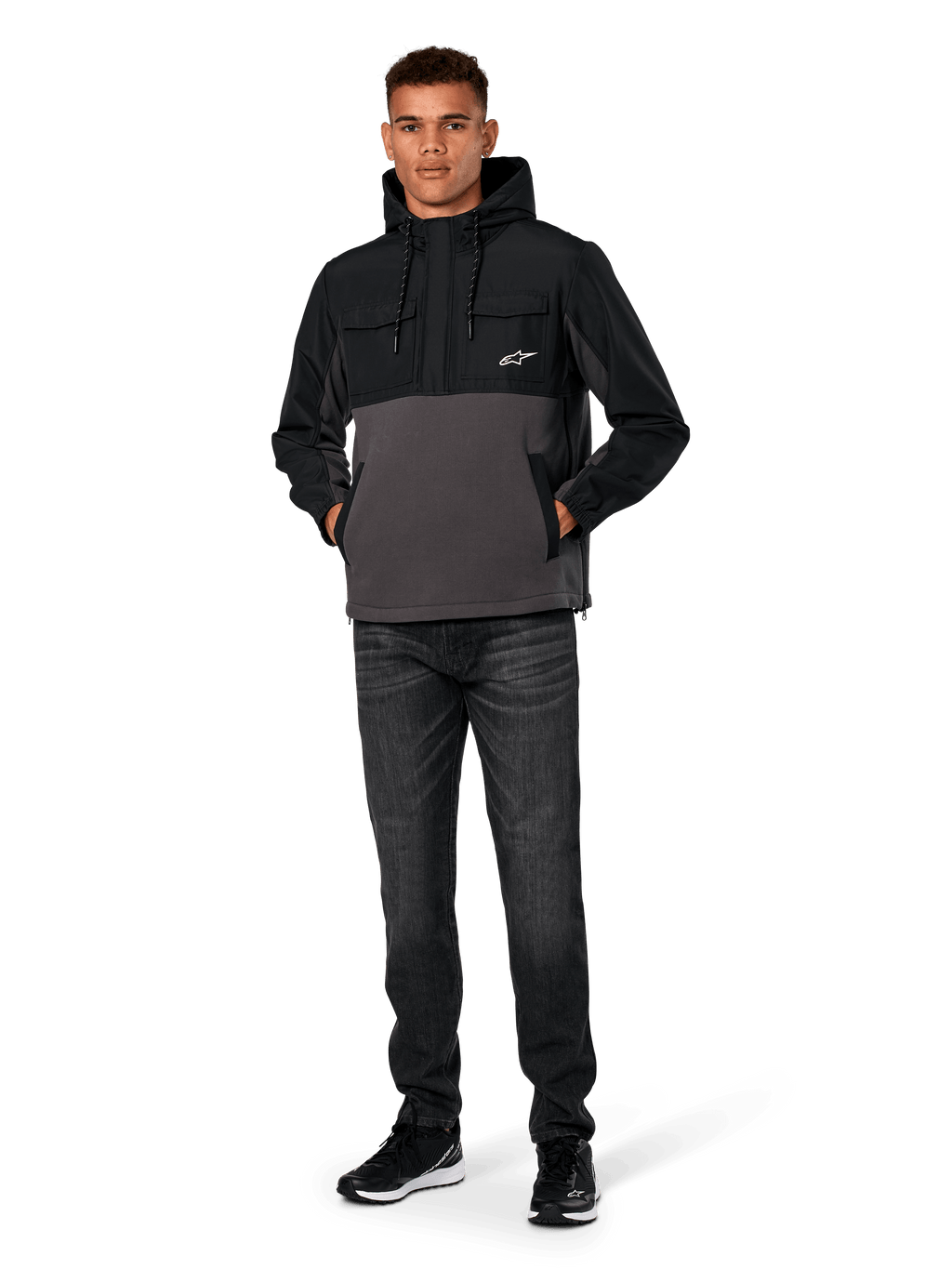 Veste Hybride Alpinestars Juncture, Noir et Anthracite, anorak à capuche en matériaux mixtes avec corps en polaire de toile et empiècements en ripstop, logo A-star blanc sur la poitrine, capuche avec cordon de serrage, portée par un mannequin avec un jean foncé et des baskets noires, streetwear décontracté inspiré du sport automobile